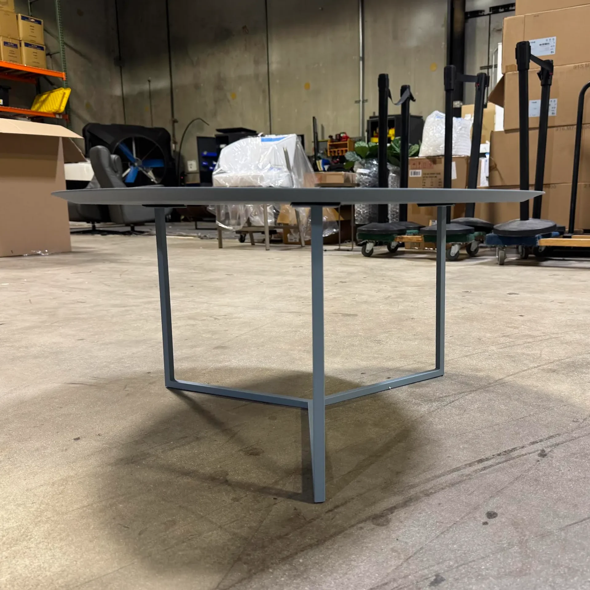 A gray, round coffee table with a square metal base in a warehouse setting.