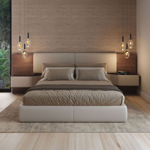 A modern bedroom with a large bed, neutral bedding, a textured headboard, floating nightstands, and warm pendant lights. A window shows green foliage.