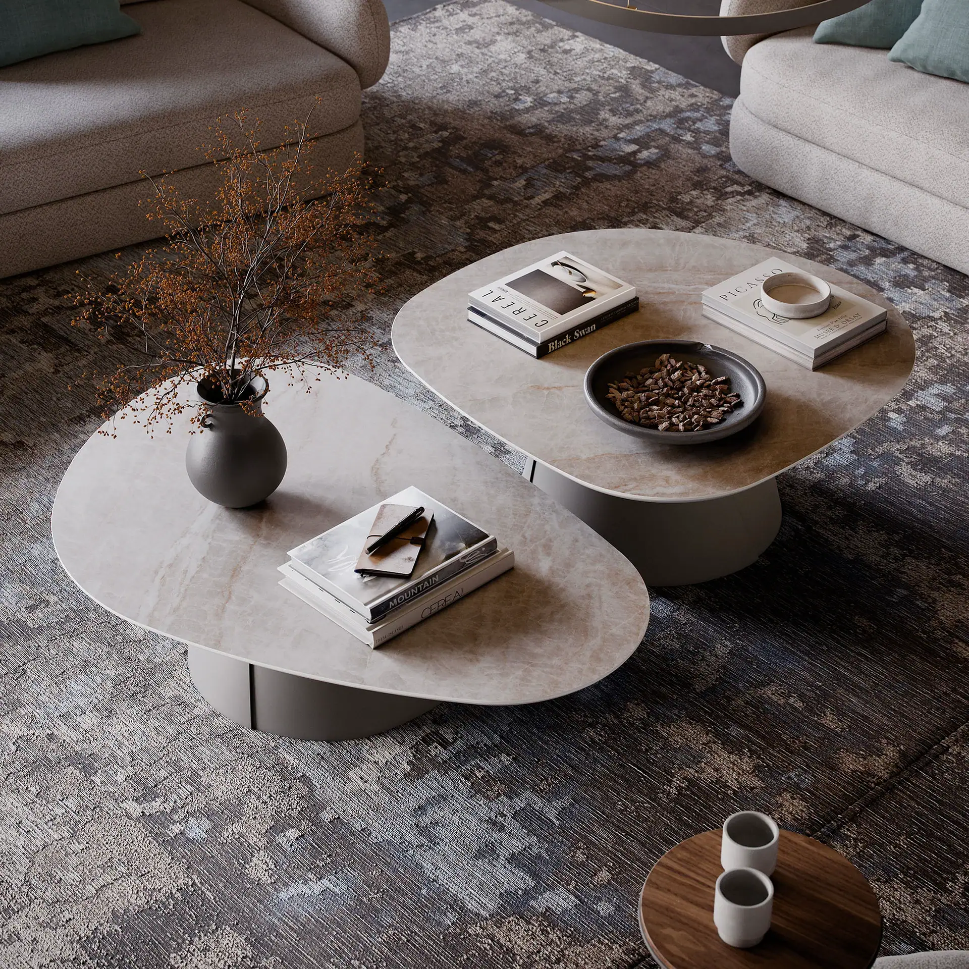 Overhead view of a modern living room with two oval coffee tables, sofas, and an abstract rug. Tables hold books, a vase with dried branches, and decorative bowls.