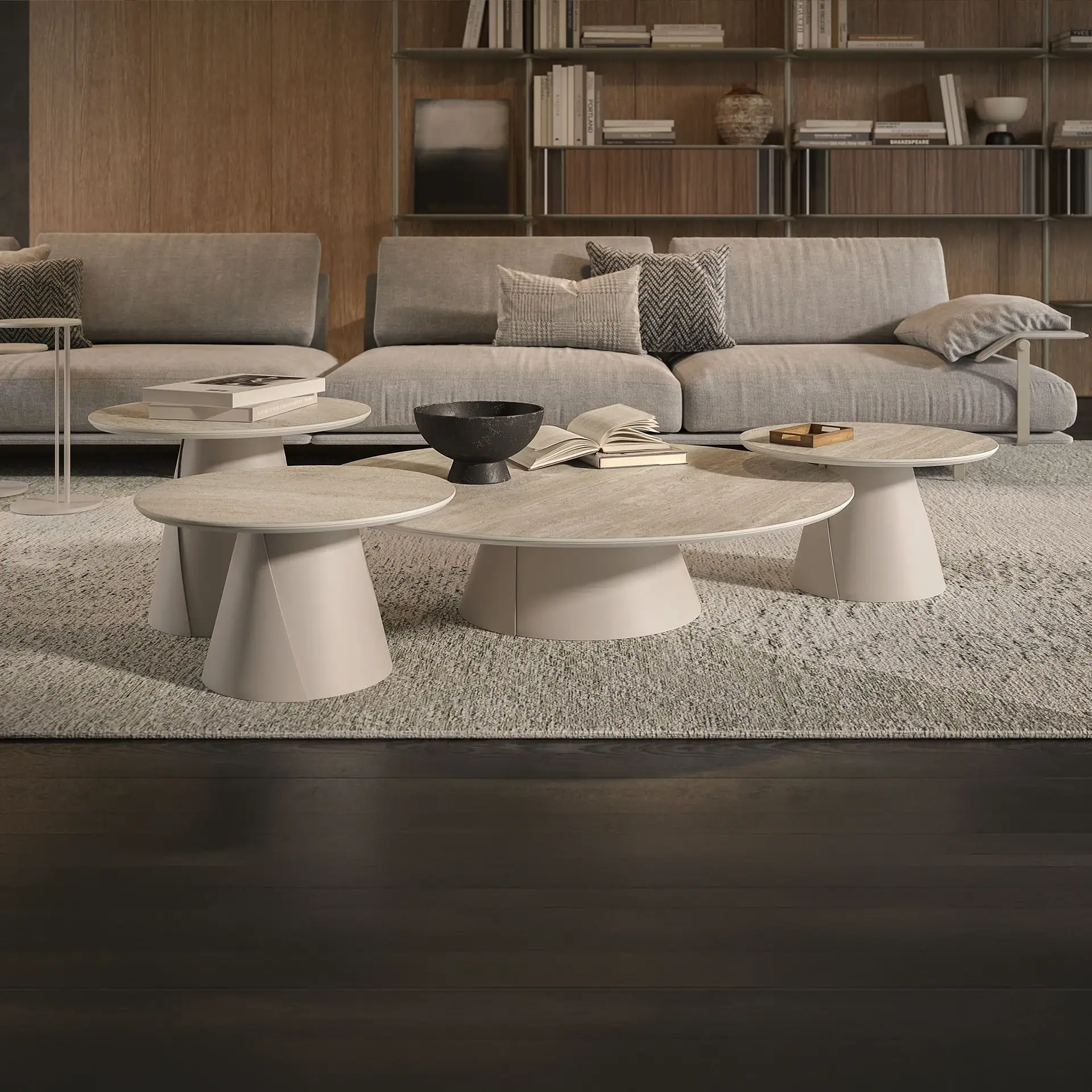 A modern living room with a light gray sofa, three round coffee tables, and a large bookshelf filled with books and decorative items.