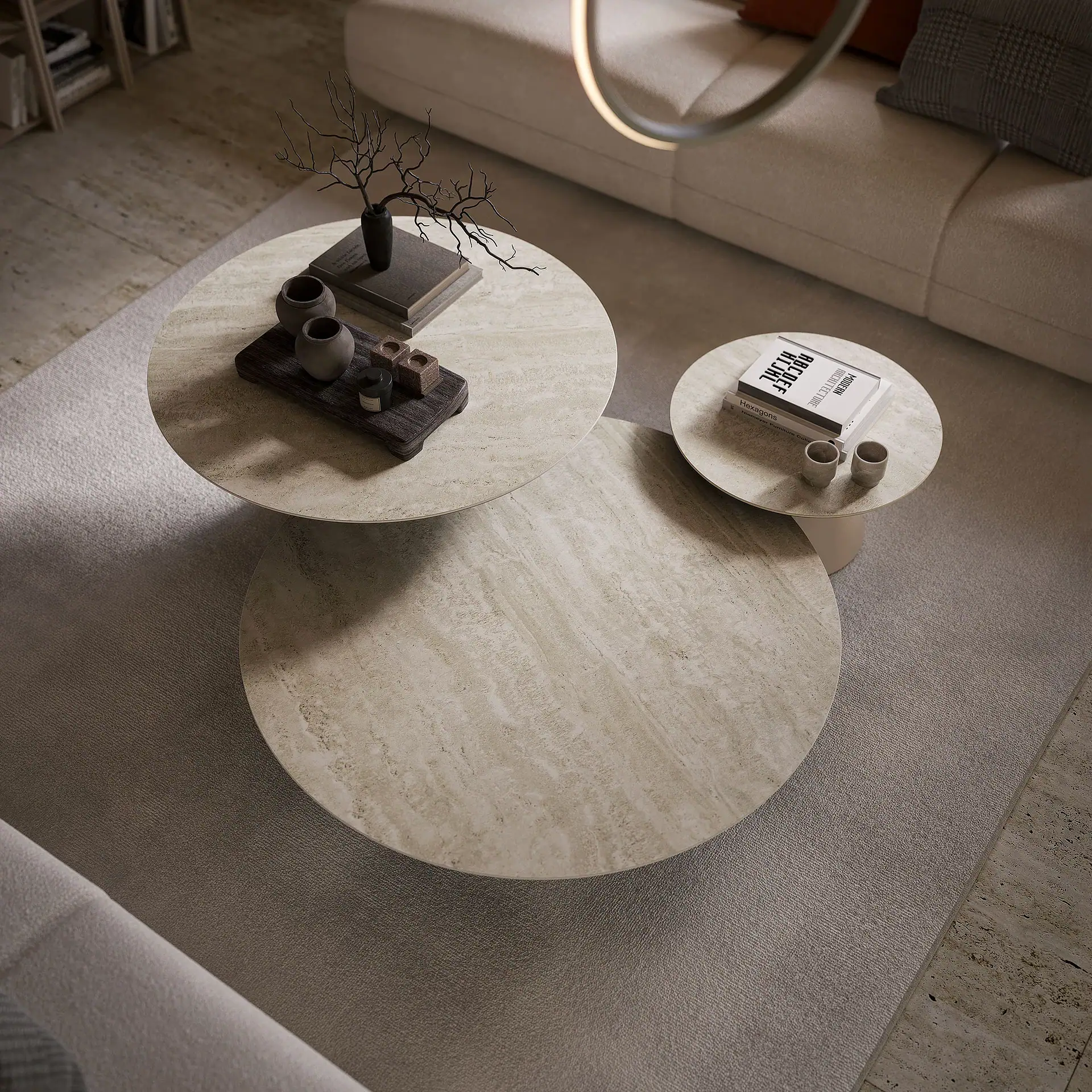 Three round, light-colored stone coffee tables with minimalist decor, including books, ceramic pots, and decorative branches, arranged on a light grey rug in a modern living room.