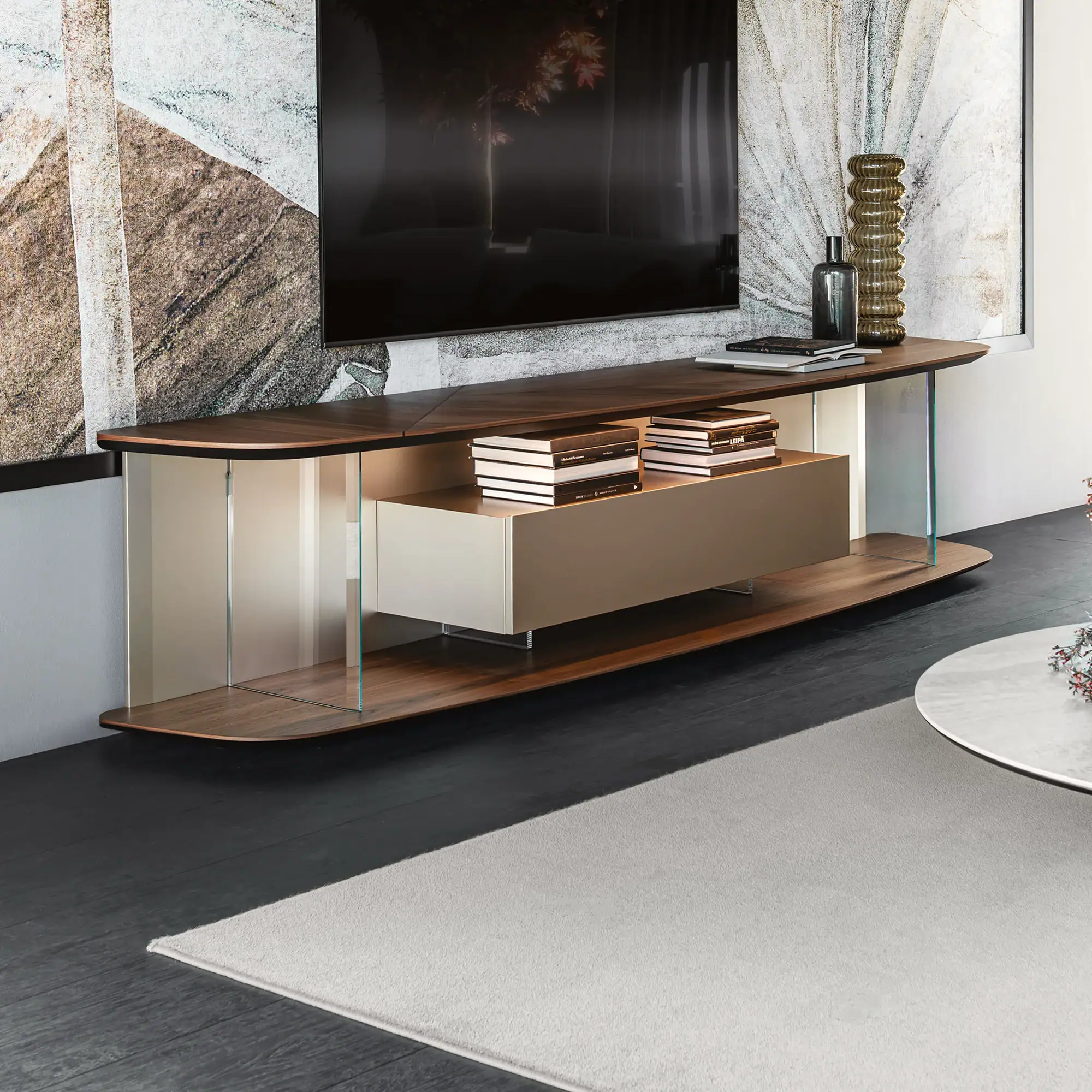 A modern media console with dark wood shelves, clear glass supports, and a light-colored floating cabinet. A flat-screen TV is mounted above it, and decorative items and books are displayed on the shelves.