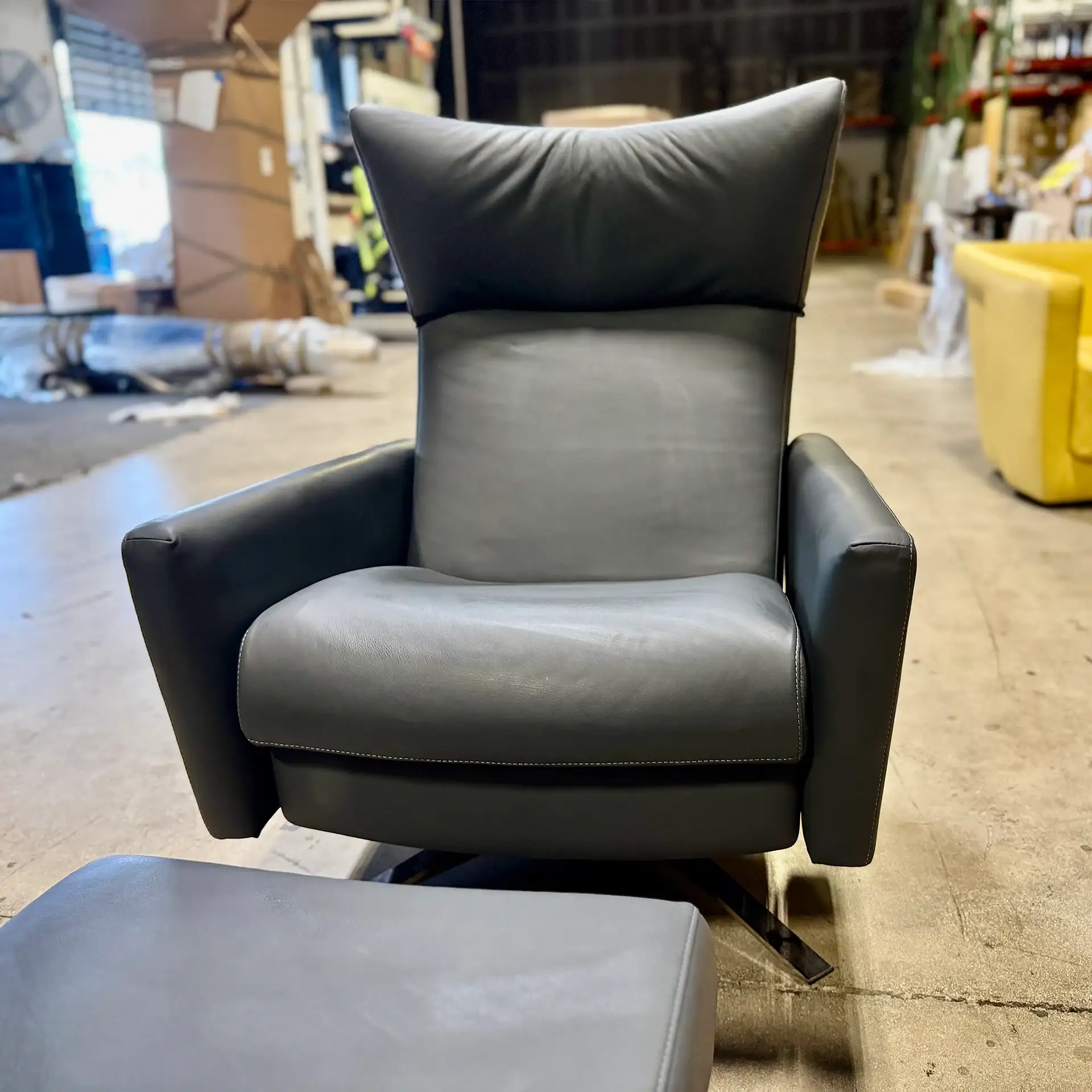 Modern black leather armchair with matching ottoman in warehouse setting.