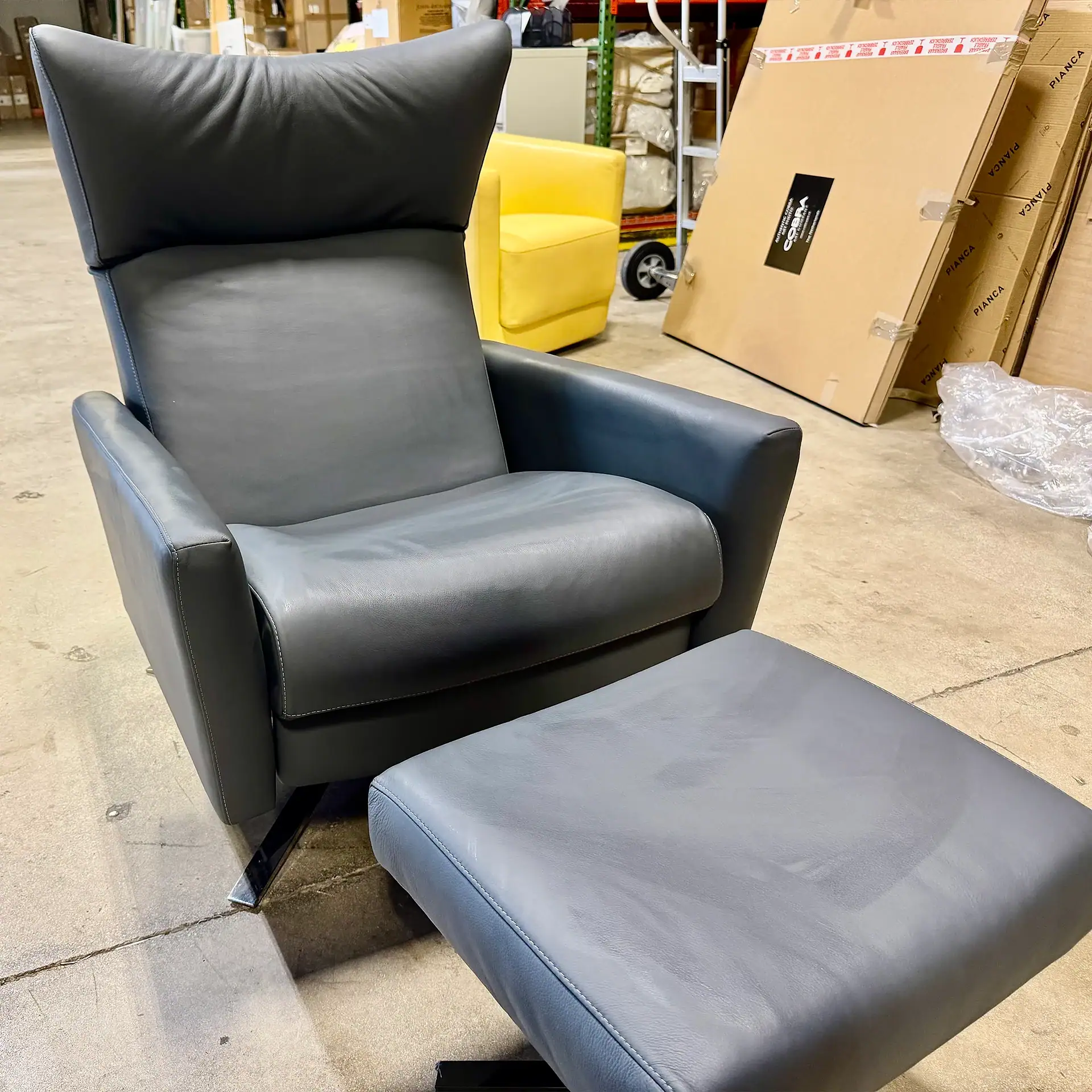 Black leather armchair with matching ottoman in warehouse setting.