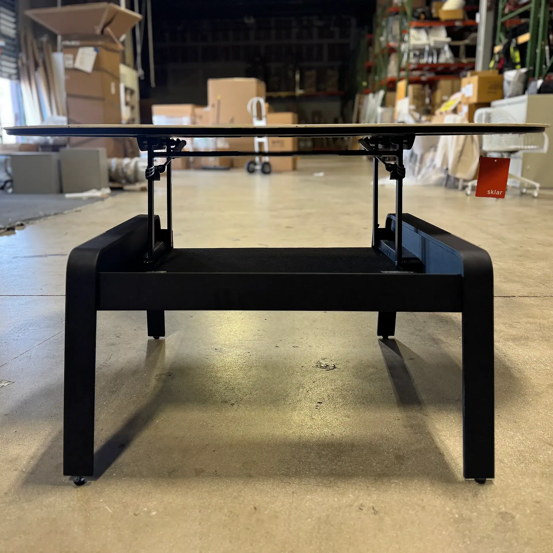 Modern lift coffee table with black base and glass top in warehouse setting.