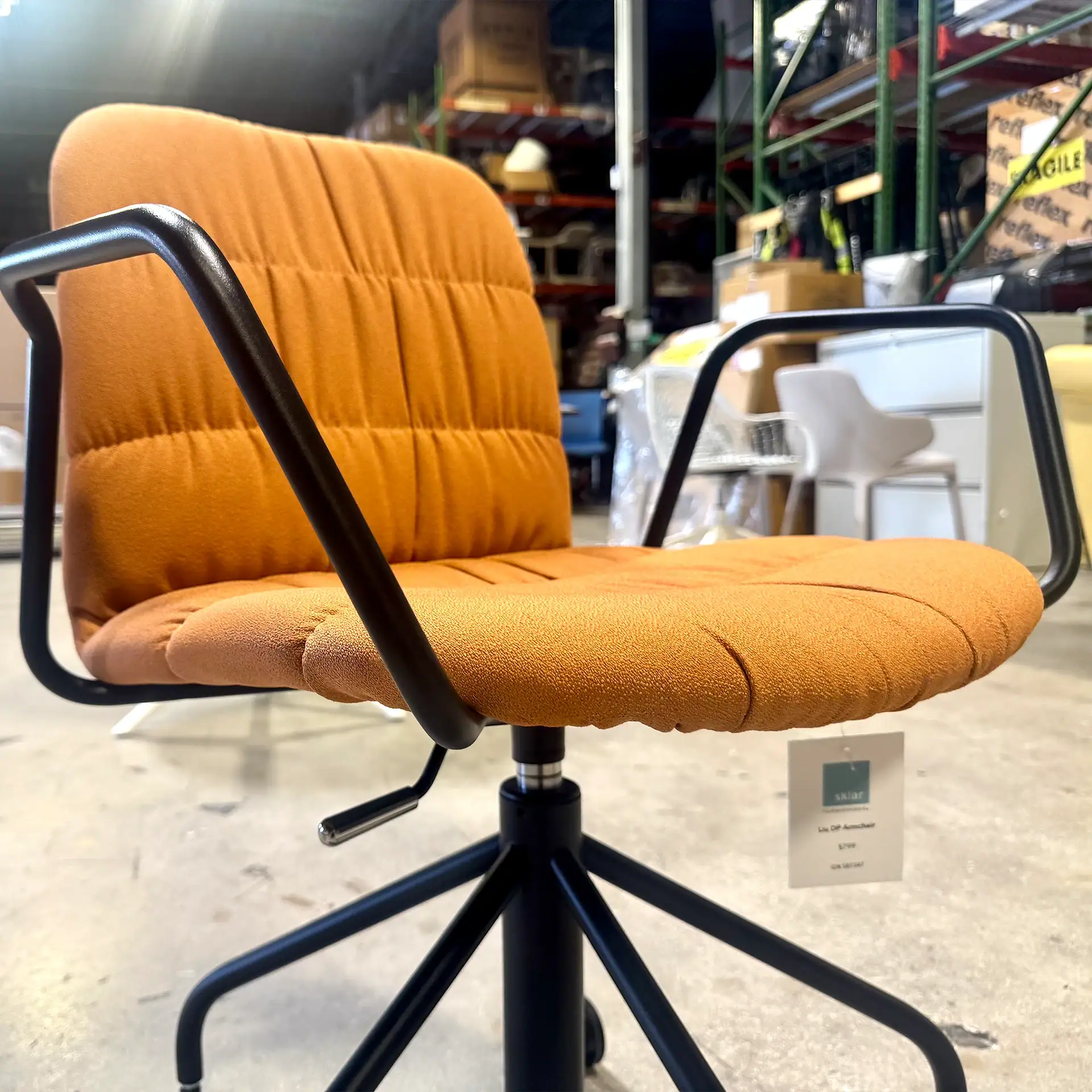 Orange Midj Liù office chair with black armrests and base in warehouse setting.