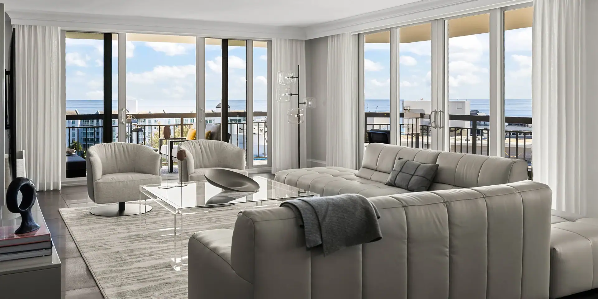Coastal living room featuring elegant white sofas, glass coffee table, and panoramic ocean views fro.