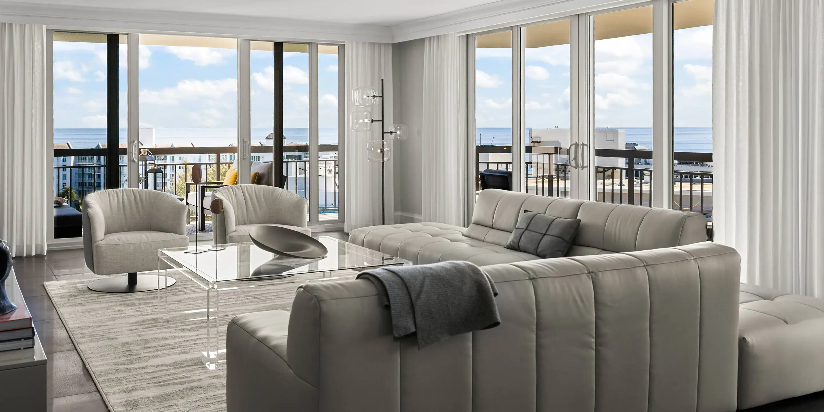 Coastal living room featuring elegant white sofas, glass coffee table, and panoramic ocean views fro.