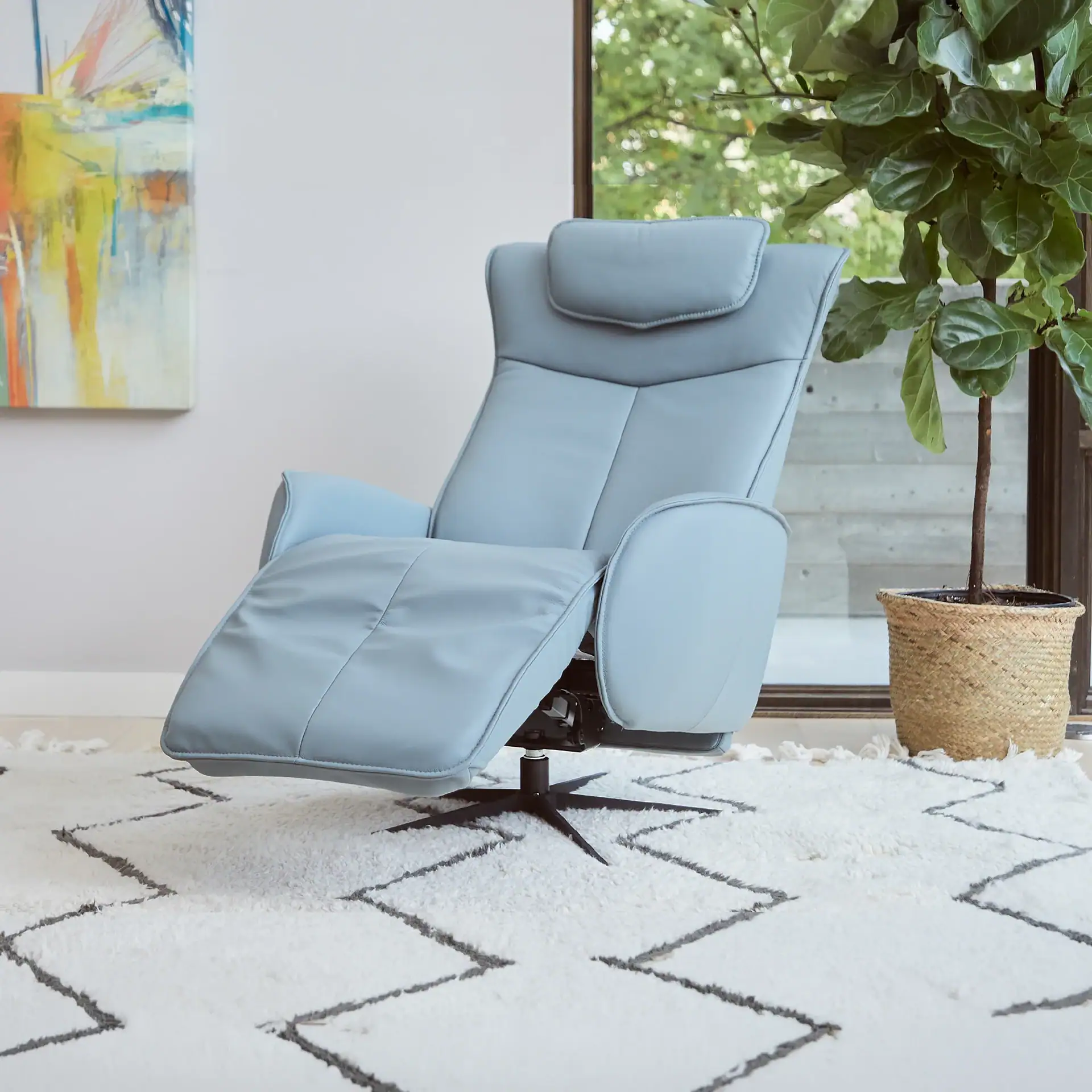 A light blue recliner chair in a reclined position on a white shag rug with a zigzag pattern. An abstract painting and a potted plant are visible in the background.