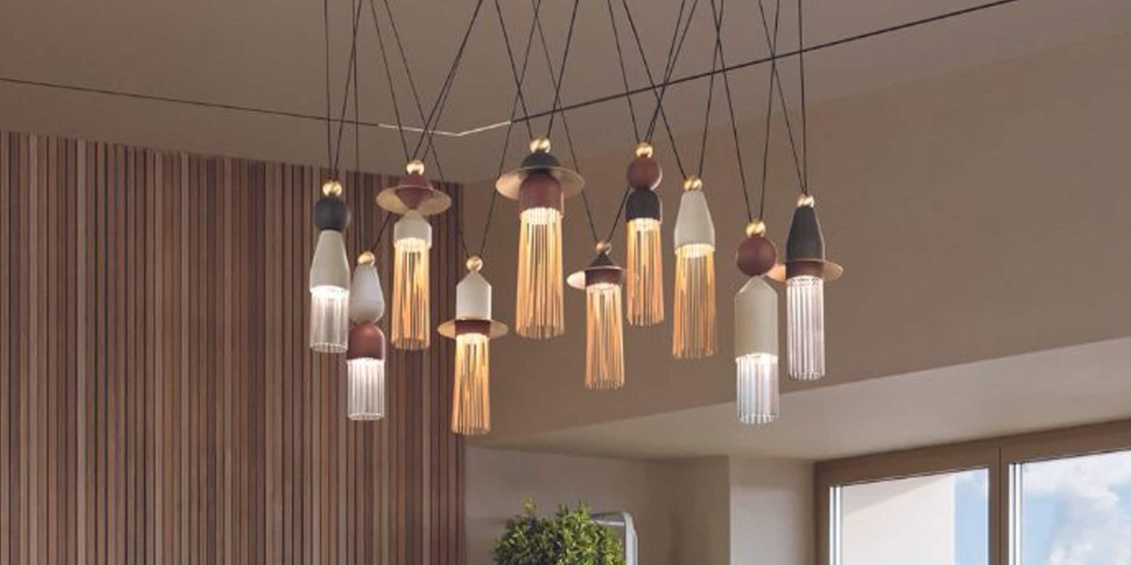 A cluster of eleven modern pendant lights with varying designs, materials, and heights, hanging in a room with a slatted wooden wall and a large window. Nappe N Series