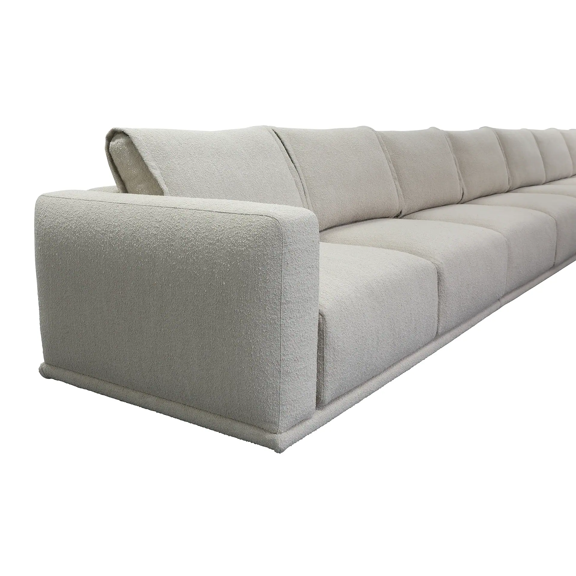 A long, light beige, textured fabric sofa with a low profile and modular cushions, against a white background.