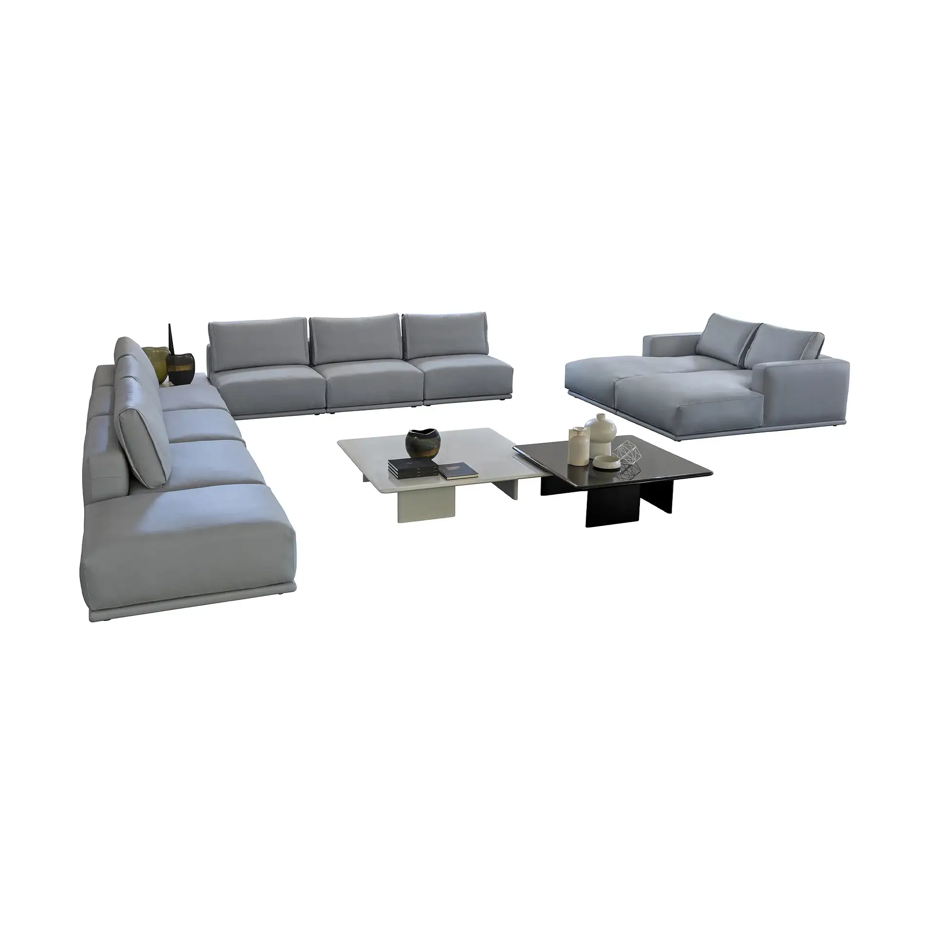 A grey modular L-shaped sofa and a grey chaise lounge sofa with two square coffee tables, one light grey and one black, adorned with decorative items, all on a white background.
