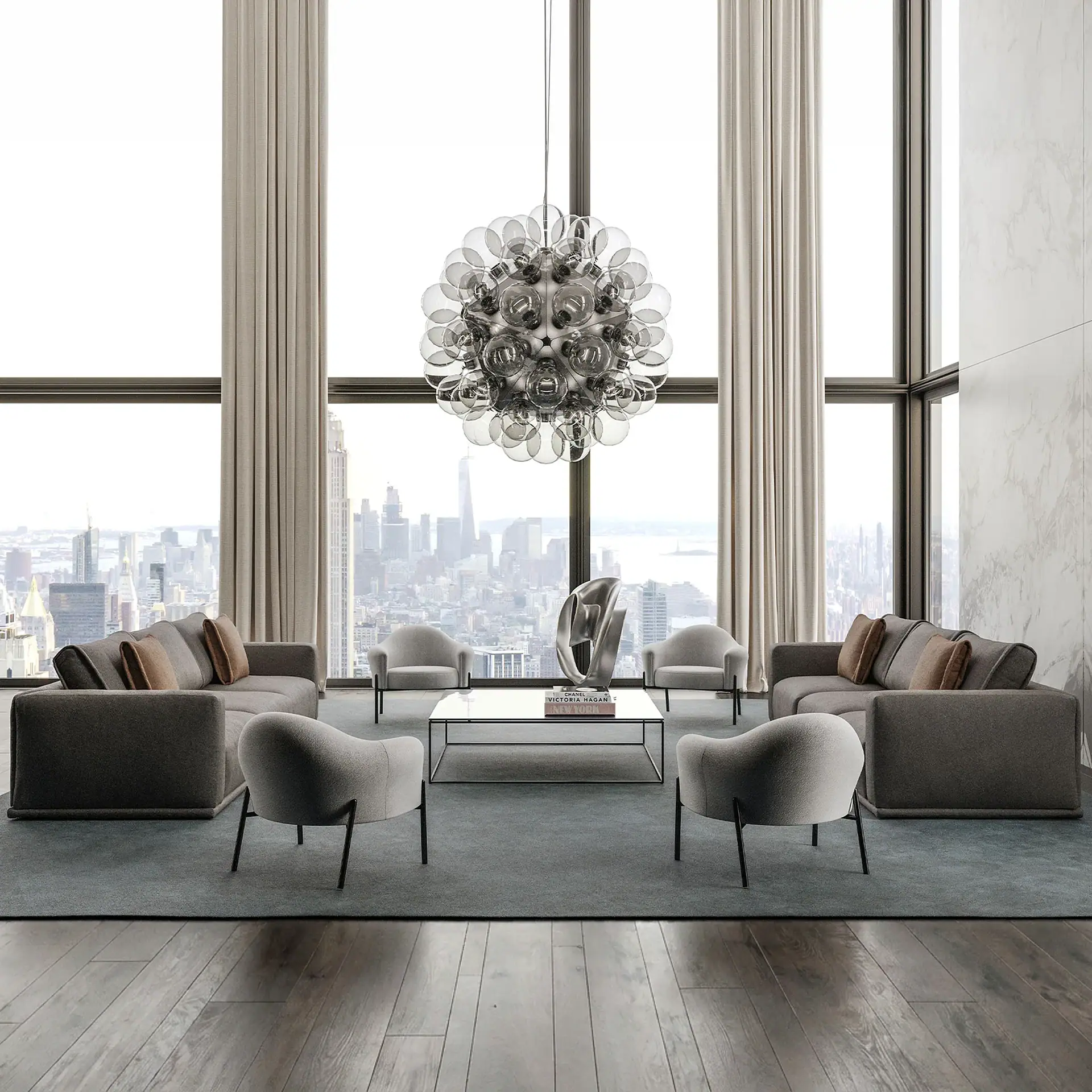 A modern living room with floor-to-ceiling windows overlooking a city skyline. The room features gray sofas, armchairs, a white coffee table with a silver sculpture, and a large spherical chandelier.