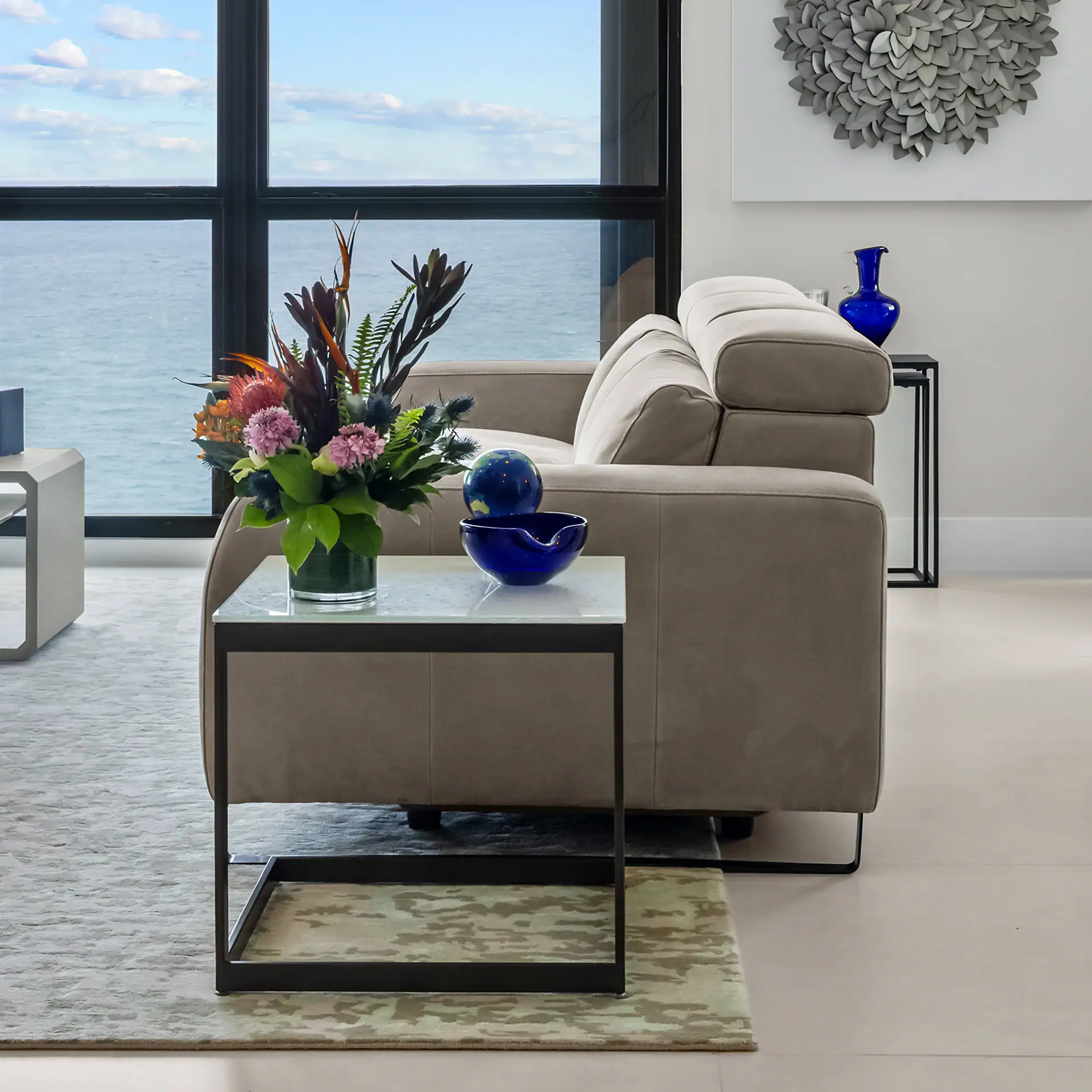 Elegant beige sofa with decorative blue vases and floral arrangement, overlooking the ocean through.