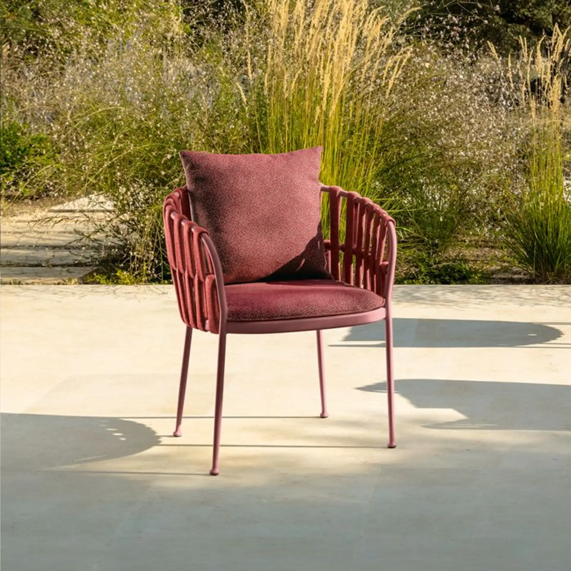 Outdoor dining armchair with a pink metal frame and plush cushion.