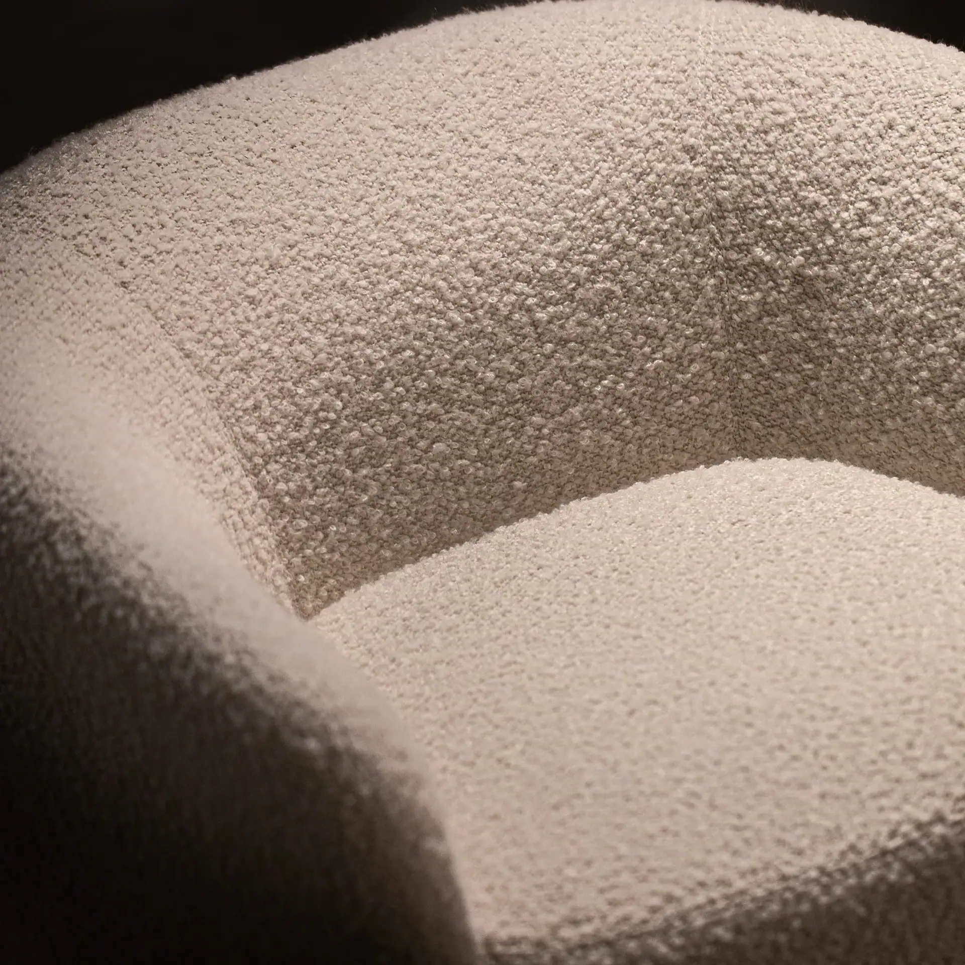 Close-up of a cream-colored bouclé upholstered chair, showing its textured fabric and rounded form under dramatic lighting.