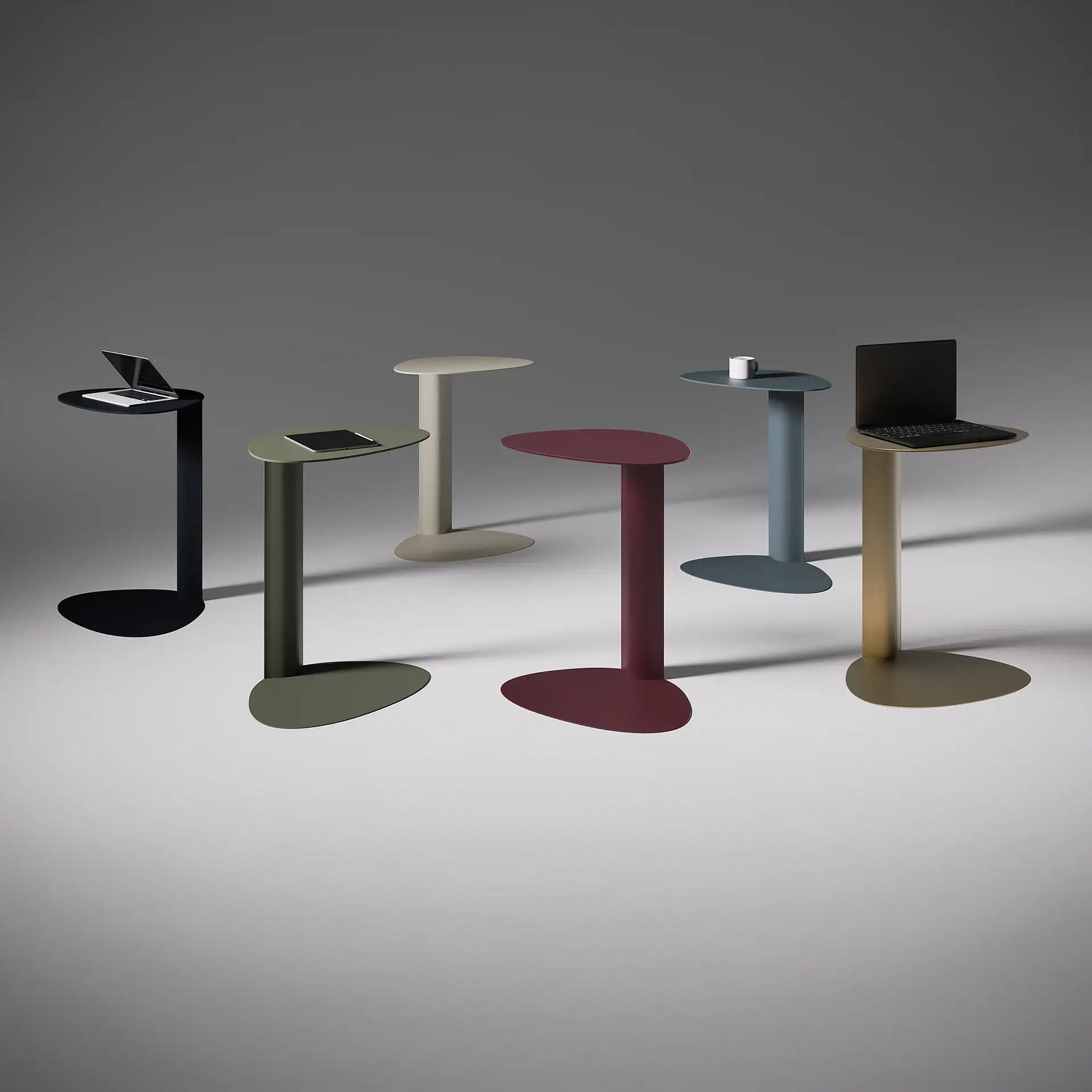 Six modern side tables in black, olive green, beige, red, blue, and gold, with laptops and a mug on some, against a grey background.