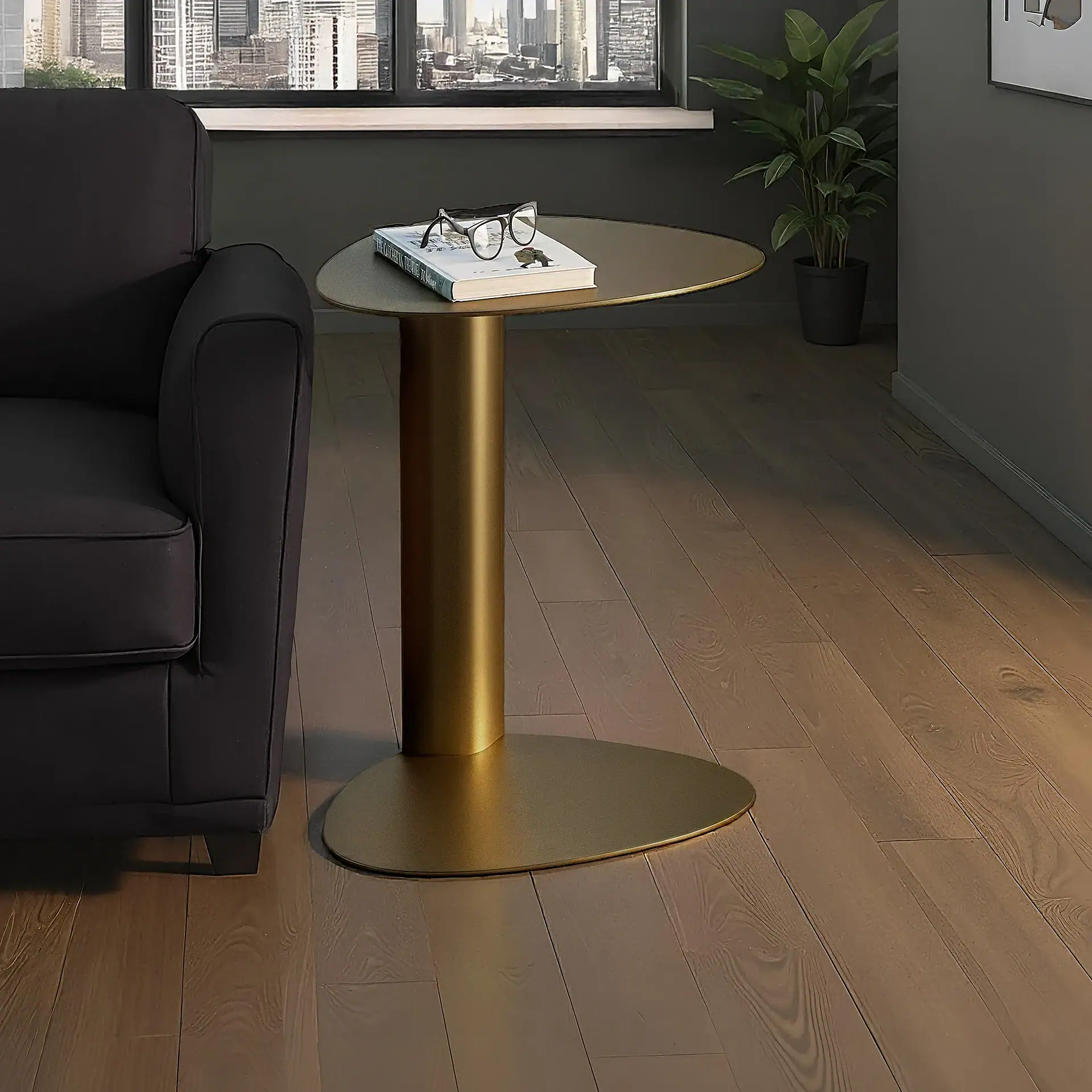 A dark gray sofa and a golden side table with a book and eyeglasses, set against a window with a cityscape view.