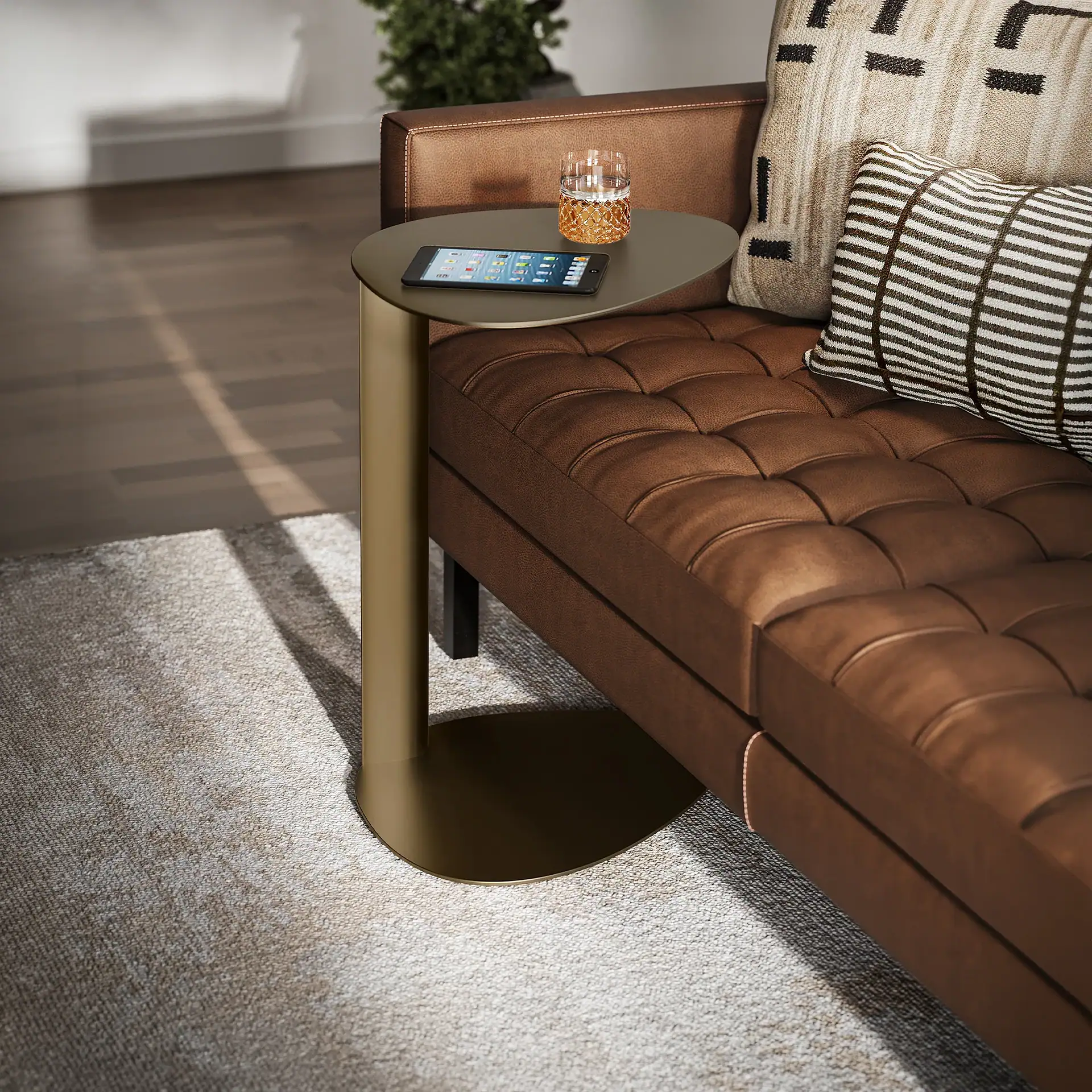A brown tufted leather sofa with decorative pillows next to an olive green C-shaped side table holding a tablet and a glass. Sunlight casts shadows on the rug.