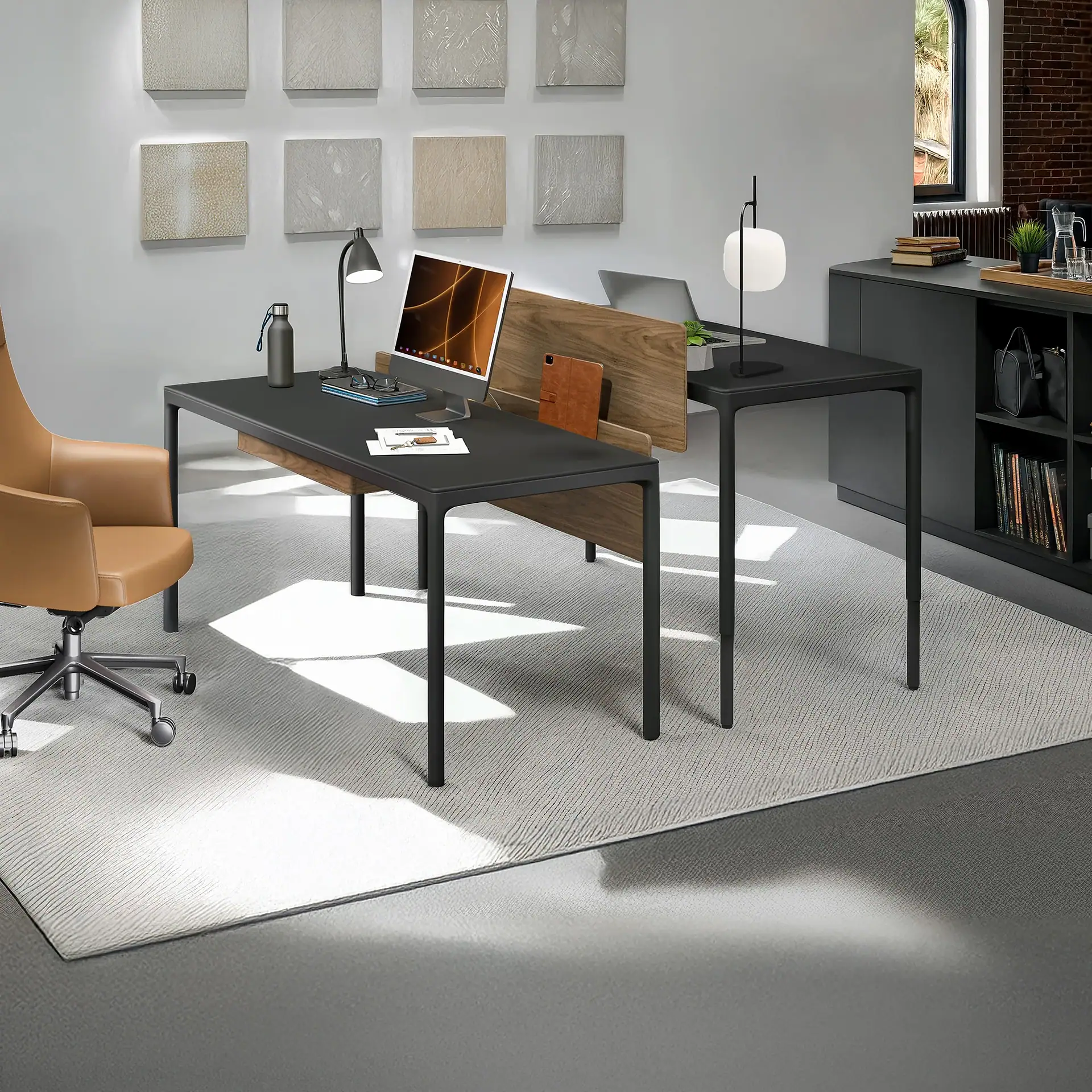 A modern office workspace featuring two dark grey desks, a tan leather office chair, and a light grey textured rug. Desks are equipped with monitors, lamps, and office supplies. A dark grey storage cabinet with decor is visible on the right.