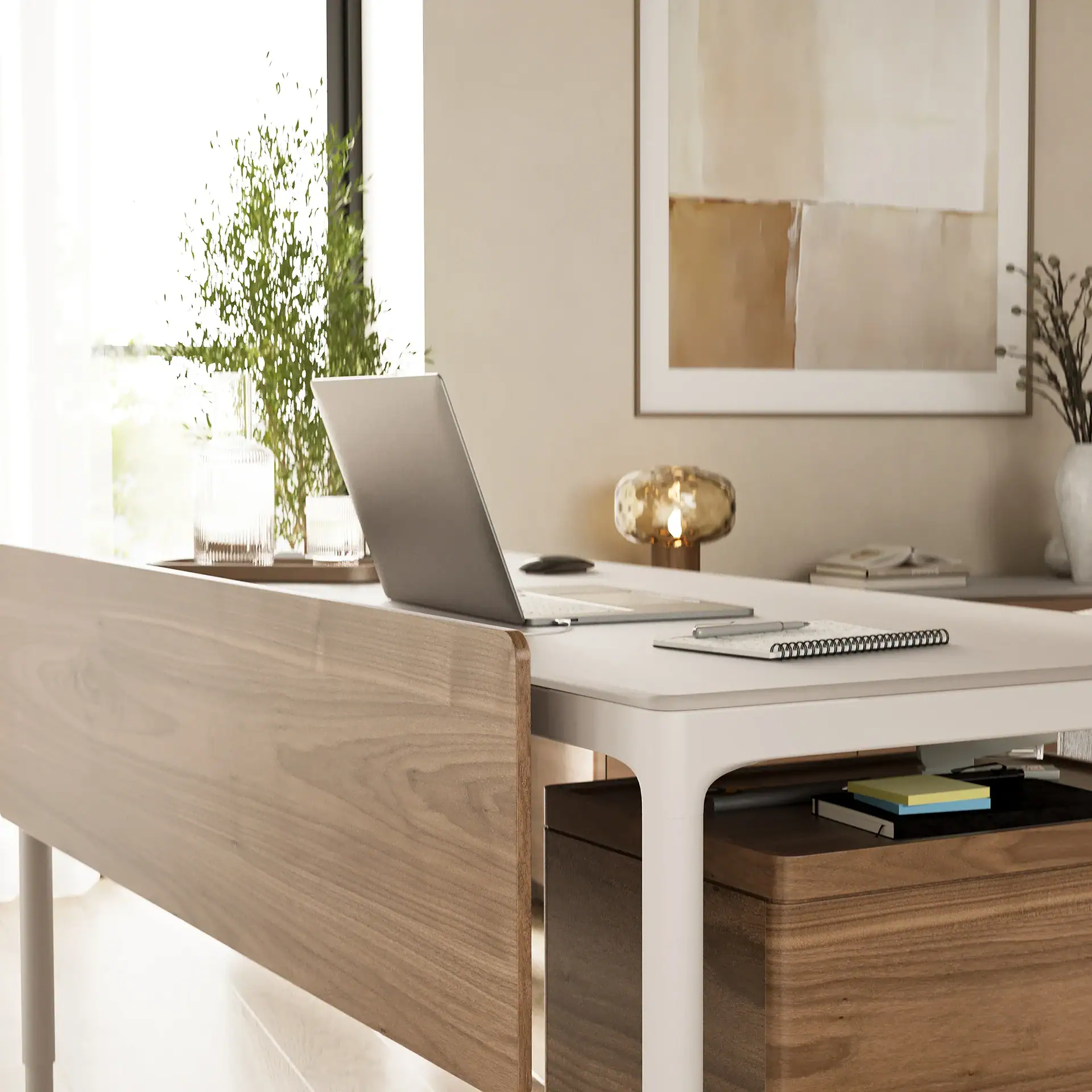 A modern home office with a white desk, silver laptop, and wooden storage unit. A potted plant, window, abstract art, and lamp are in the background.