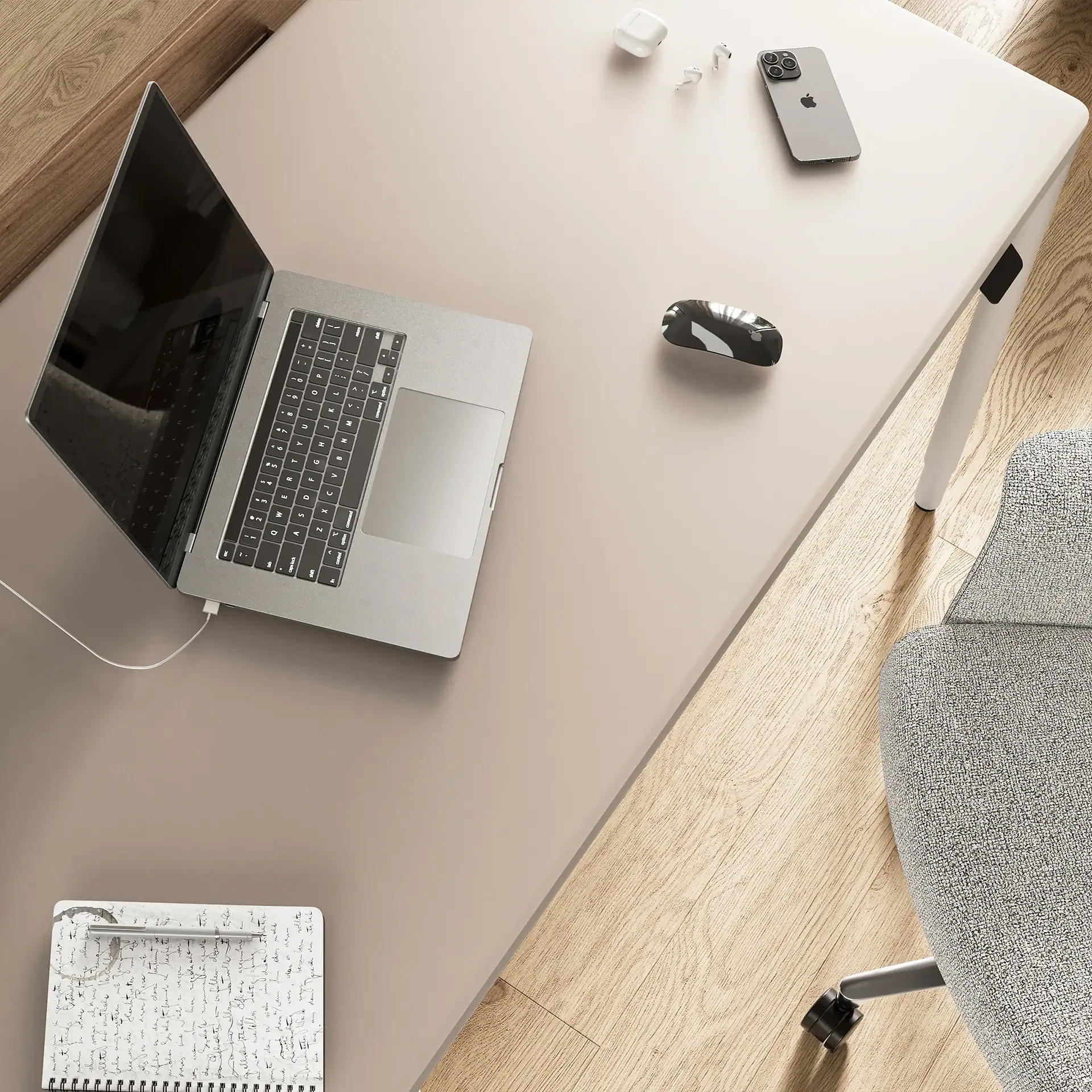 Overhead view of a modern desk with a silver laptop, iPhone, AirPods, mouse, and a notebook with a pen.