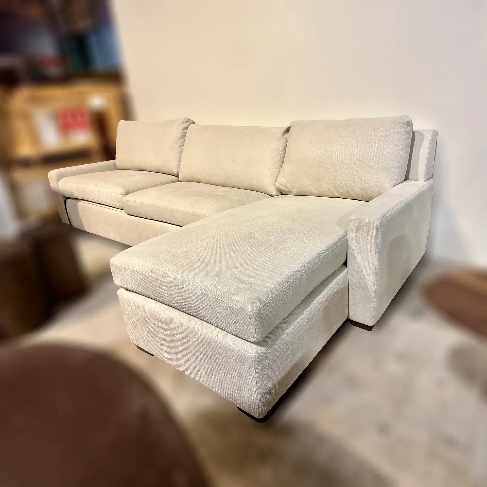 Modern beige sleeper sofa with chaise lounge in living room setting.