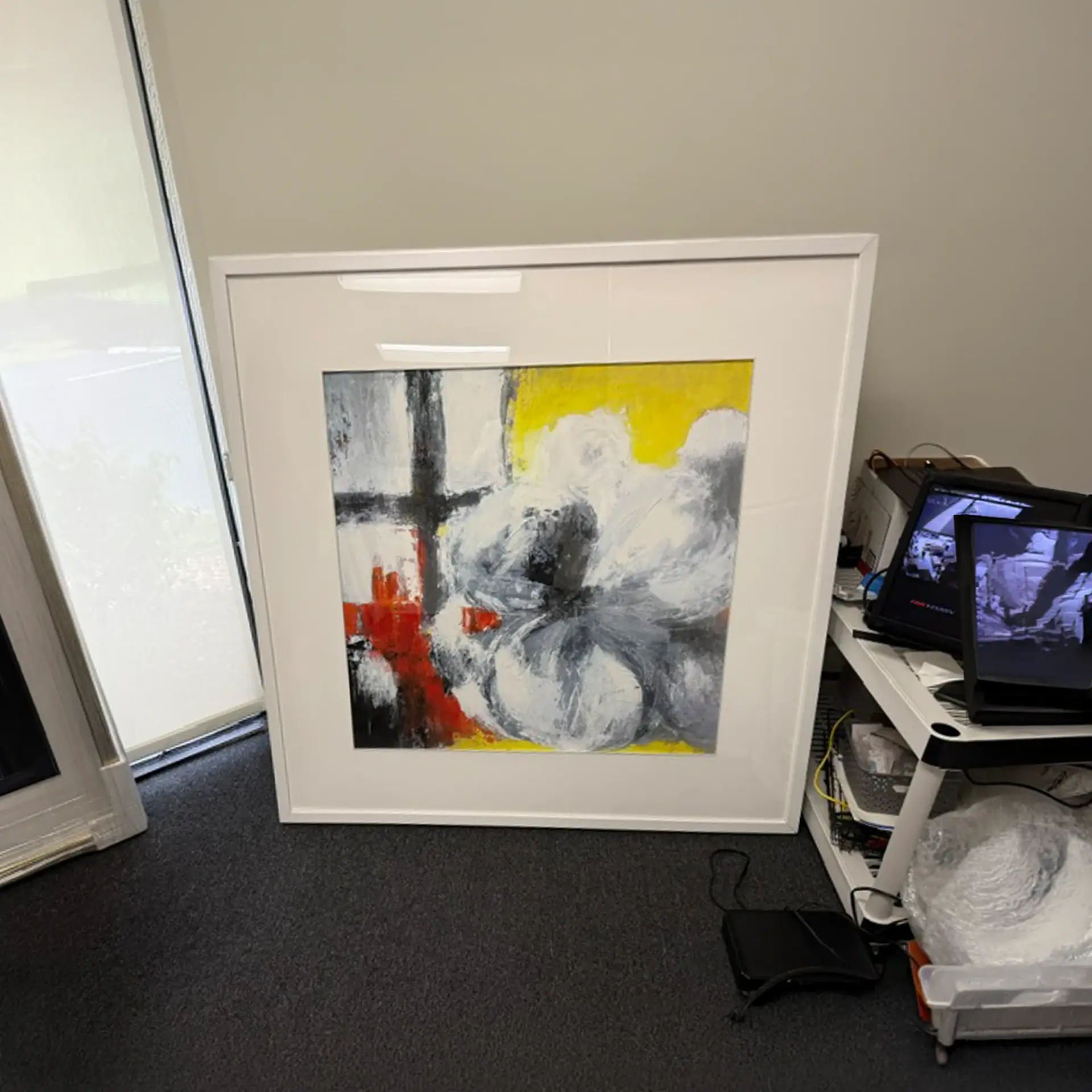 Abstract wall art with blue, yellow, black, and red colors in a white frame.