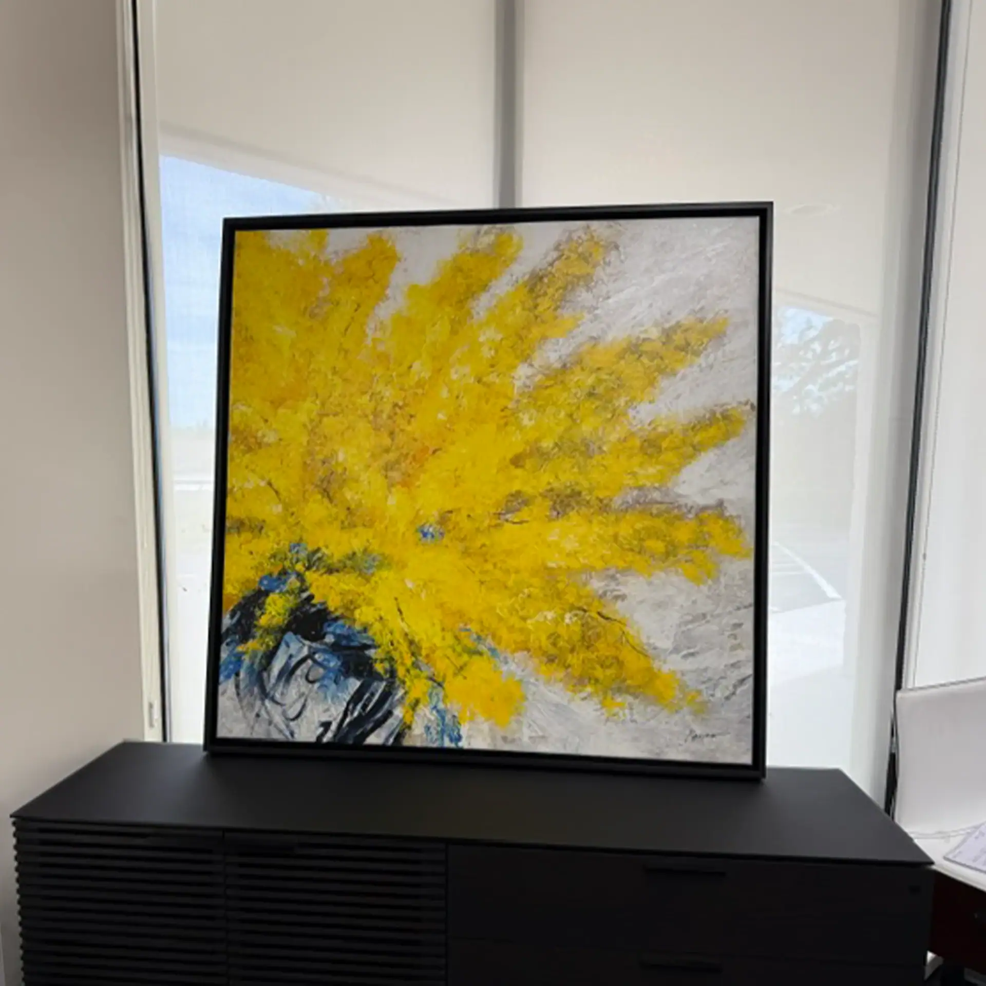 Abstract yellow and gray wall art displayed on a black stand in modern interior.