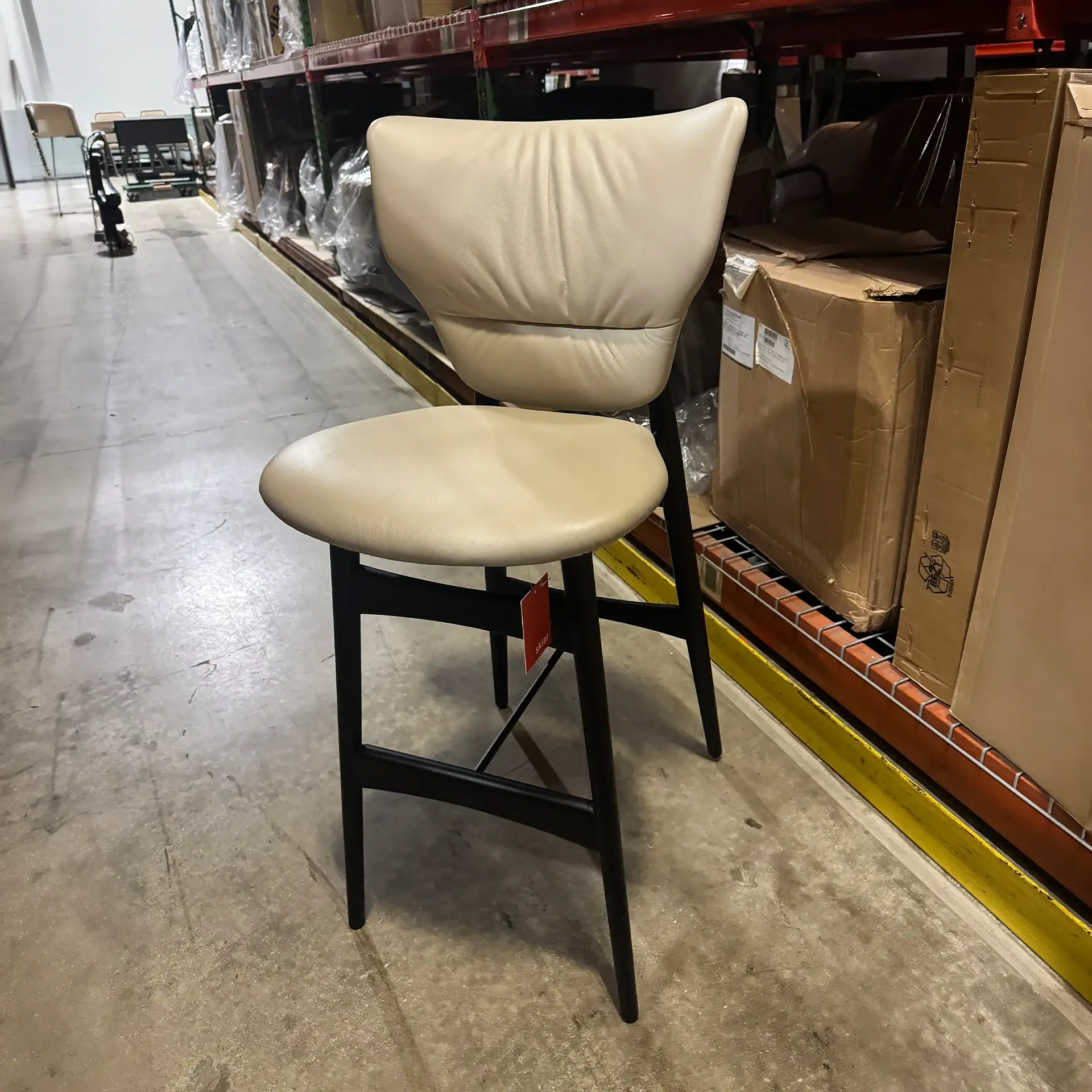 Modern Dumbo stool with cream upholstery and black wooden legs.