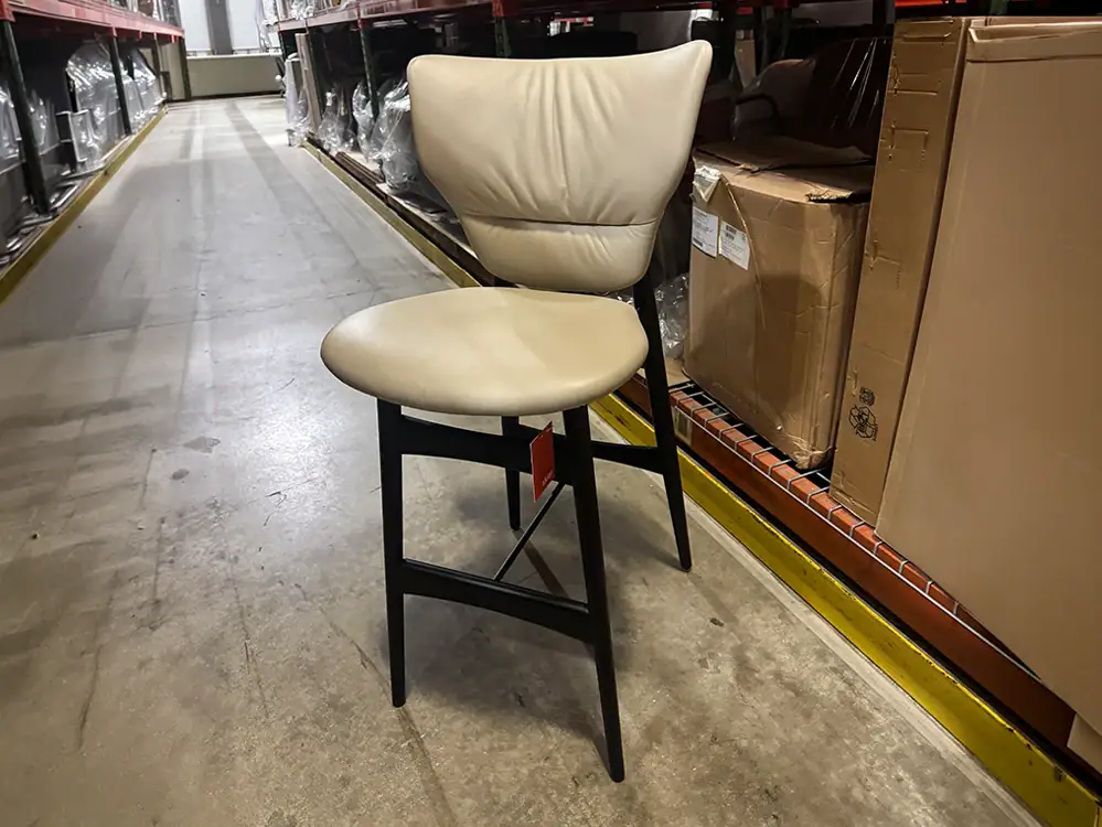 Modern Dumbo Stool with cream upholstered seat and black wooden legs.