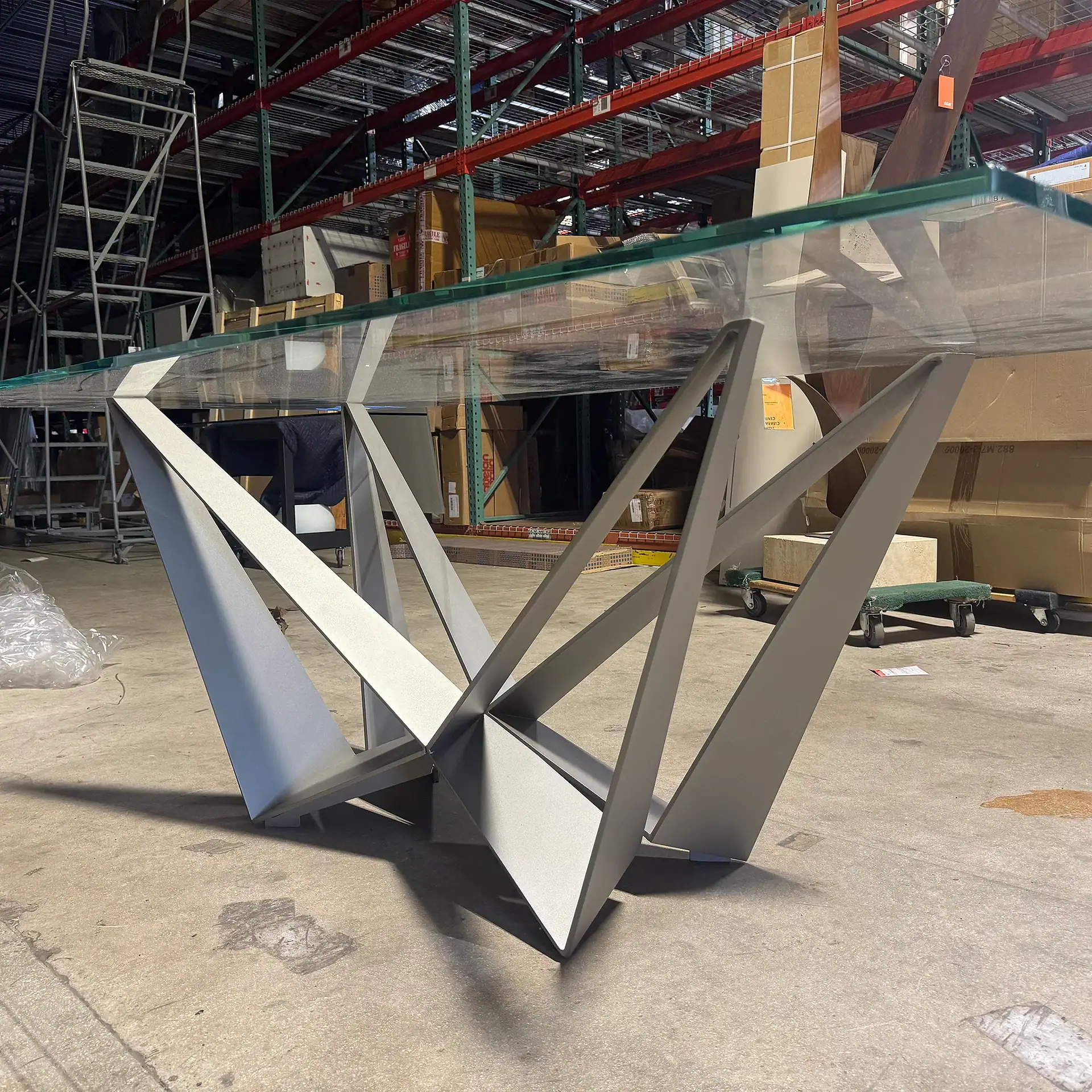 Contemporary glass dining table with geometric metal base in warehouse setting.