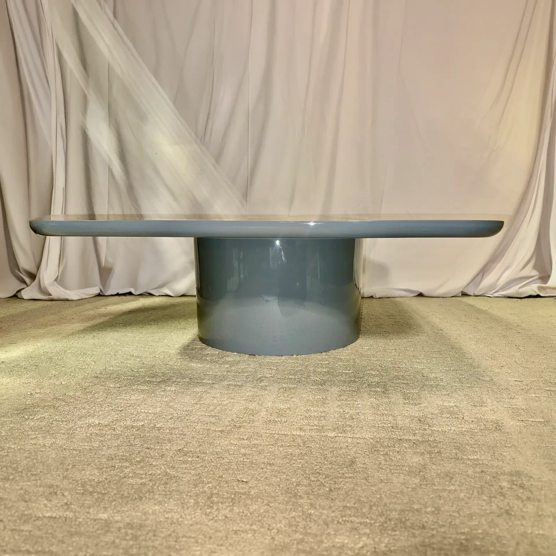 Modern grey cocktail table with round base and flat top in a neutral setting.