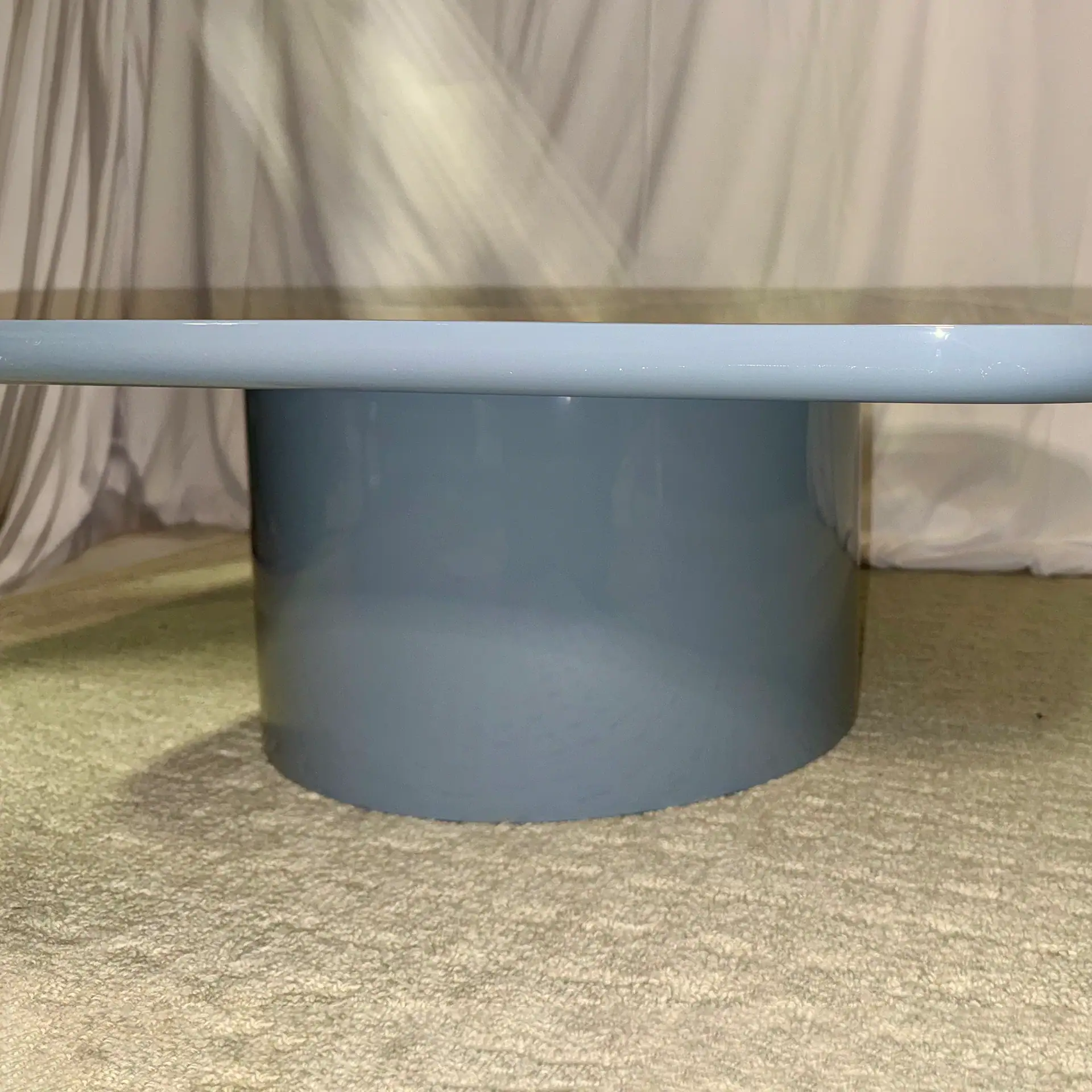 Modern blue cocktail table with cylindrical base and round top in a living room setting.