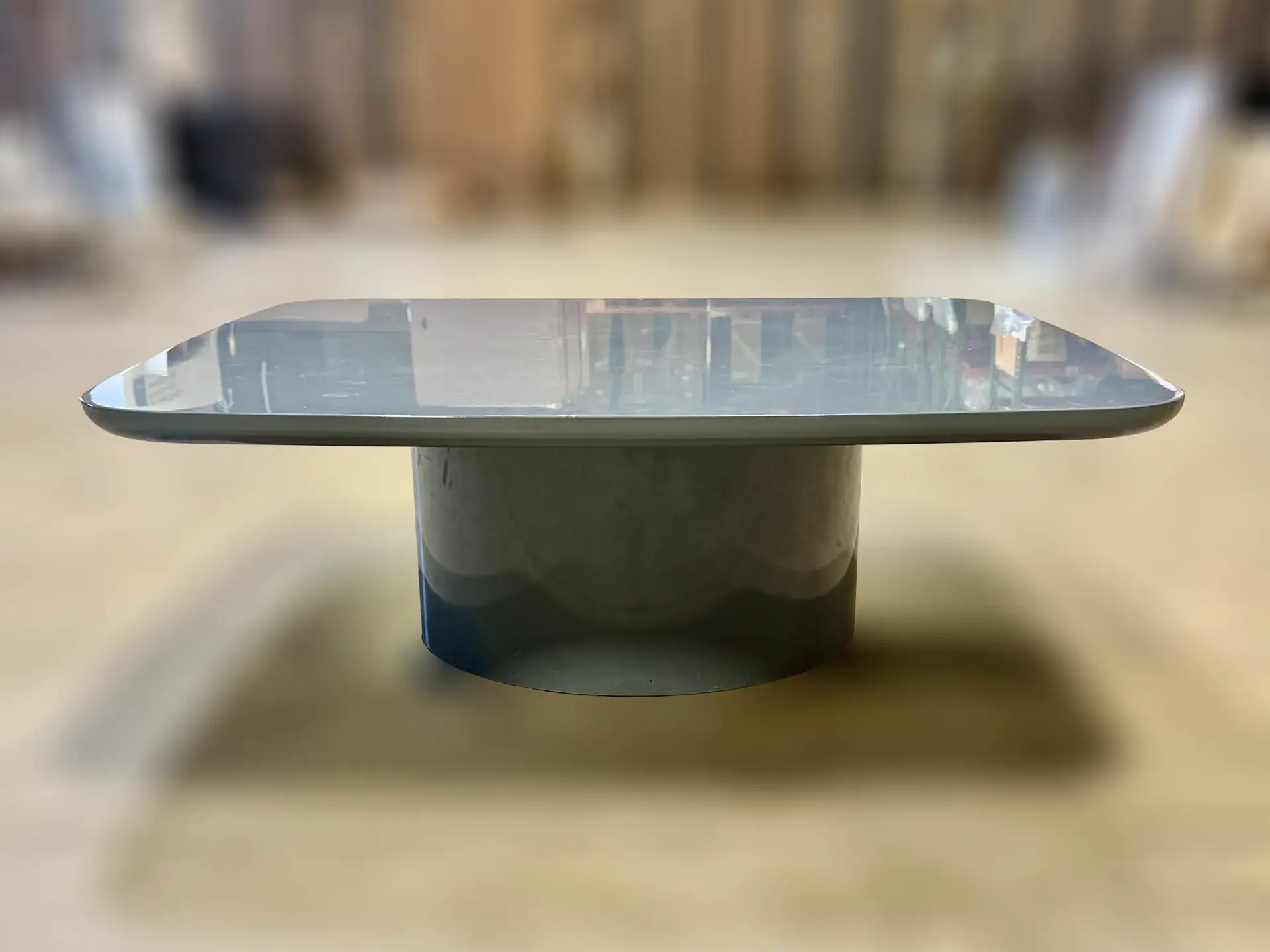 Modern glass-top cocktail table with cylindrical base in a furniture showroom.