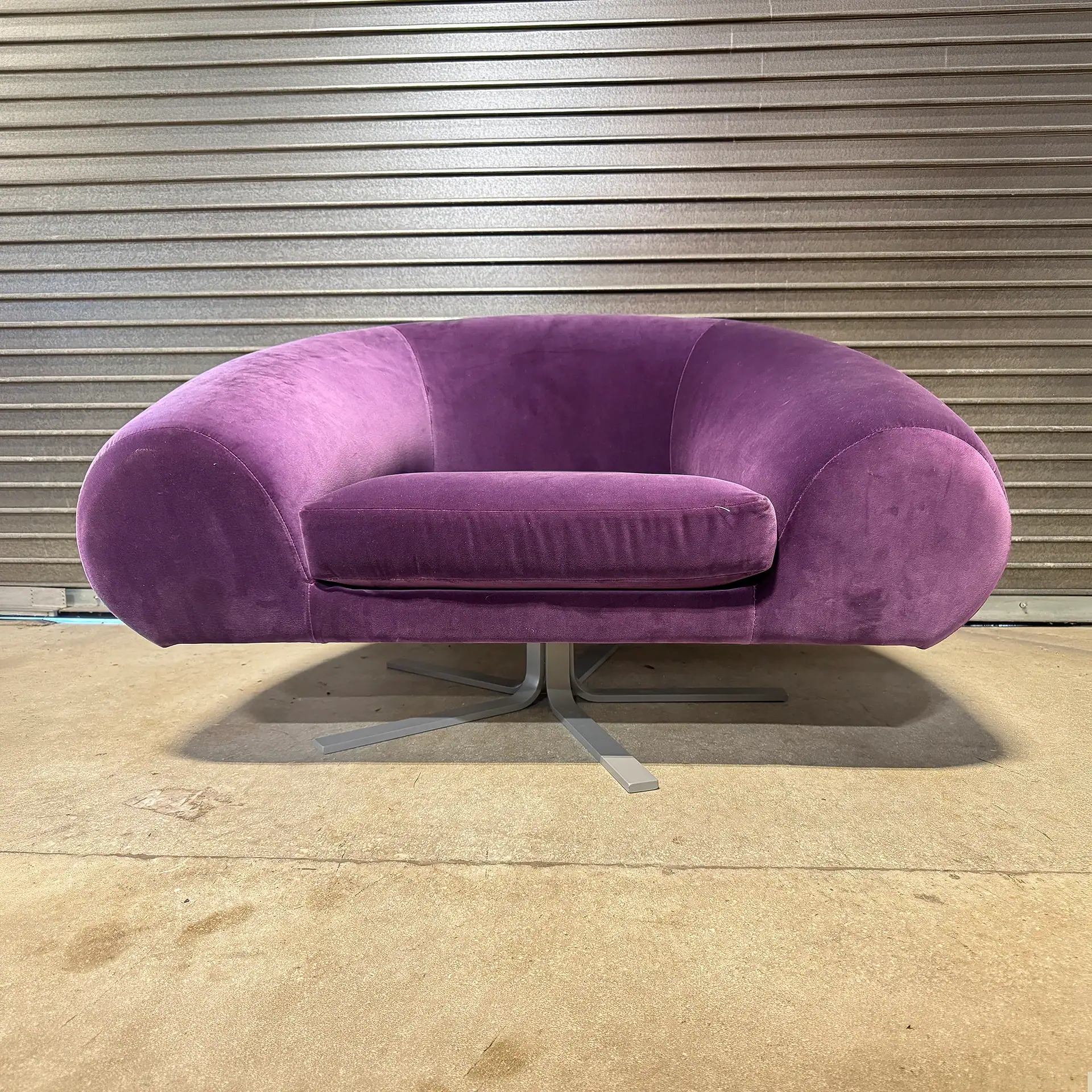 Purple lounge chair with modern design and metal base in a showroom.