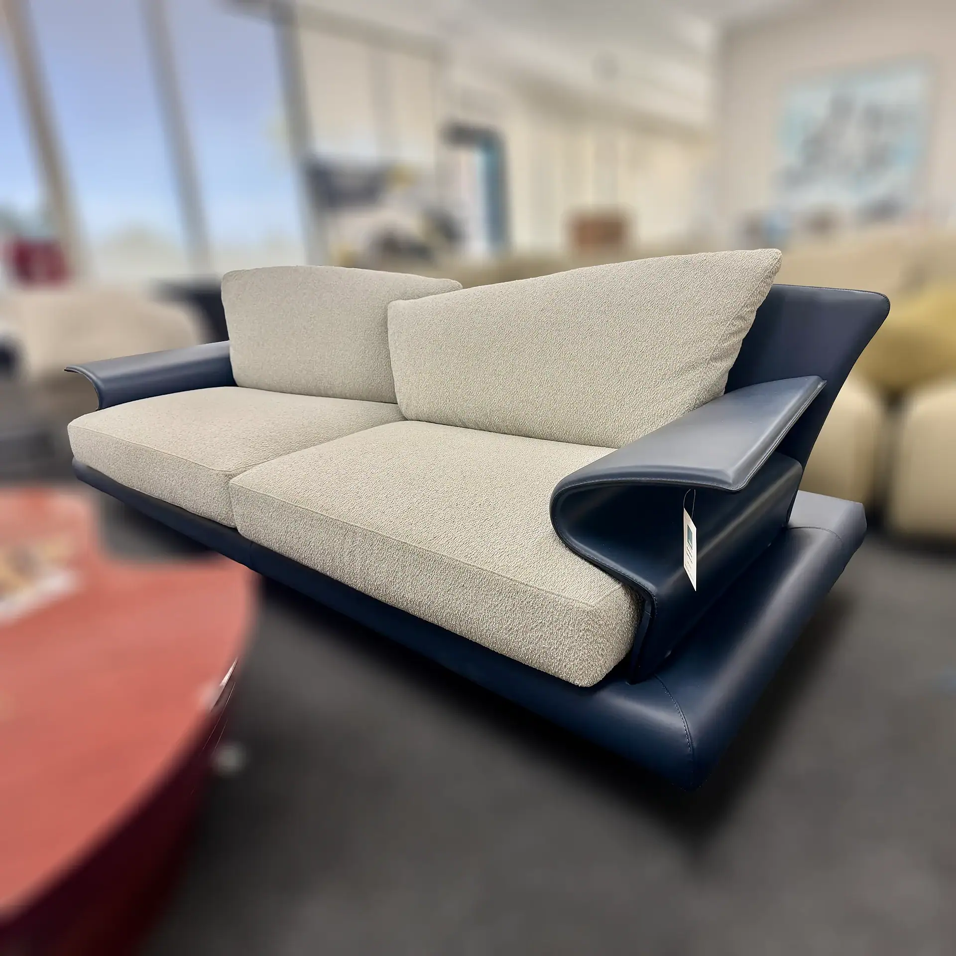 Contemporary sofa with beige cushions and dark armrests in showroom.