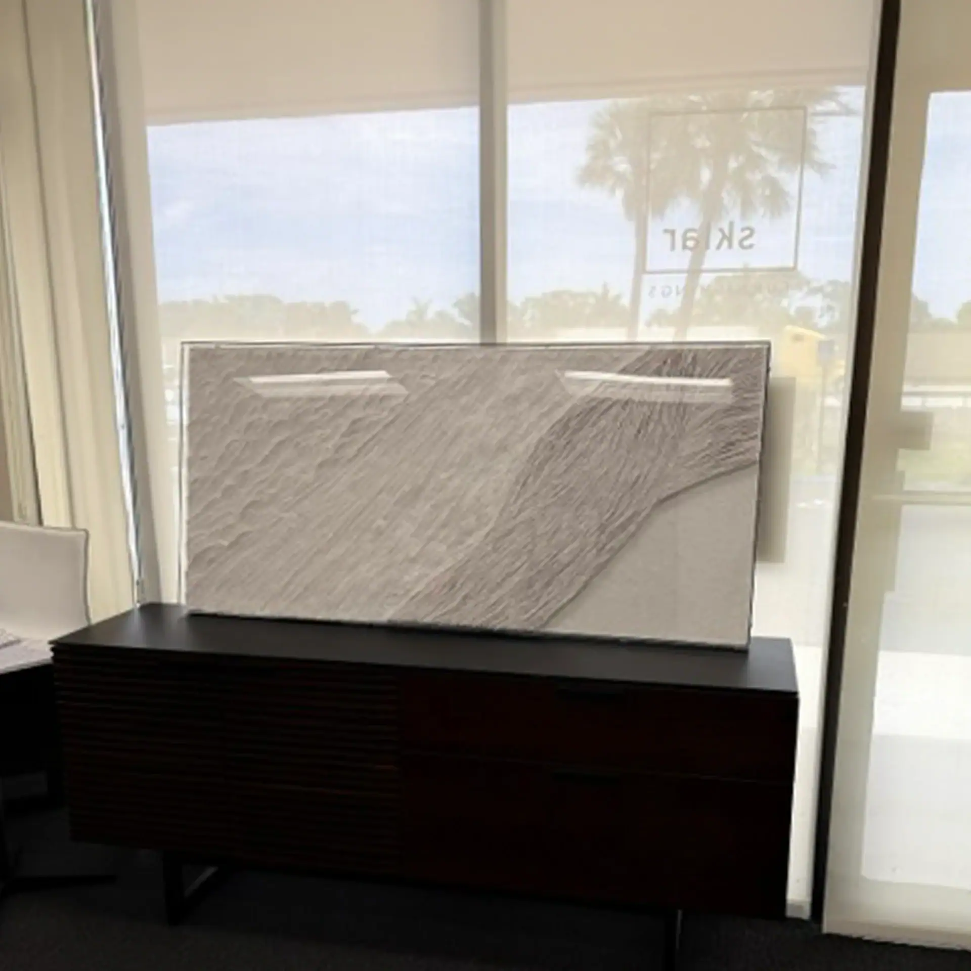 Modern wall art piece displayed on a dark wooden sideboard in a bright showroom.