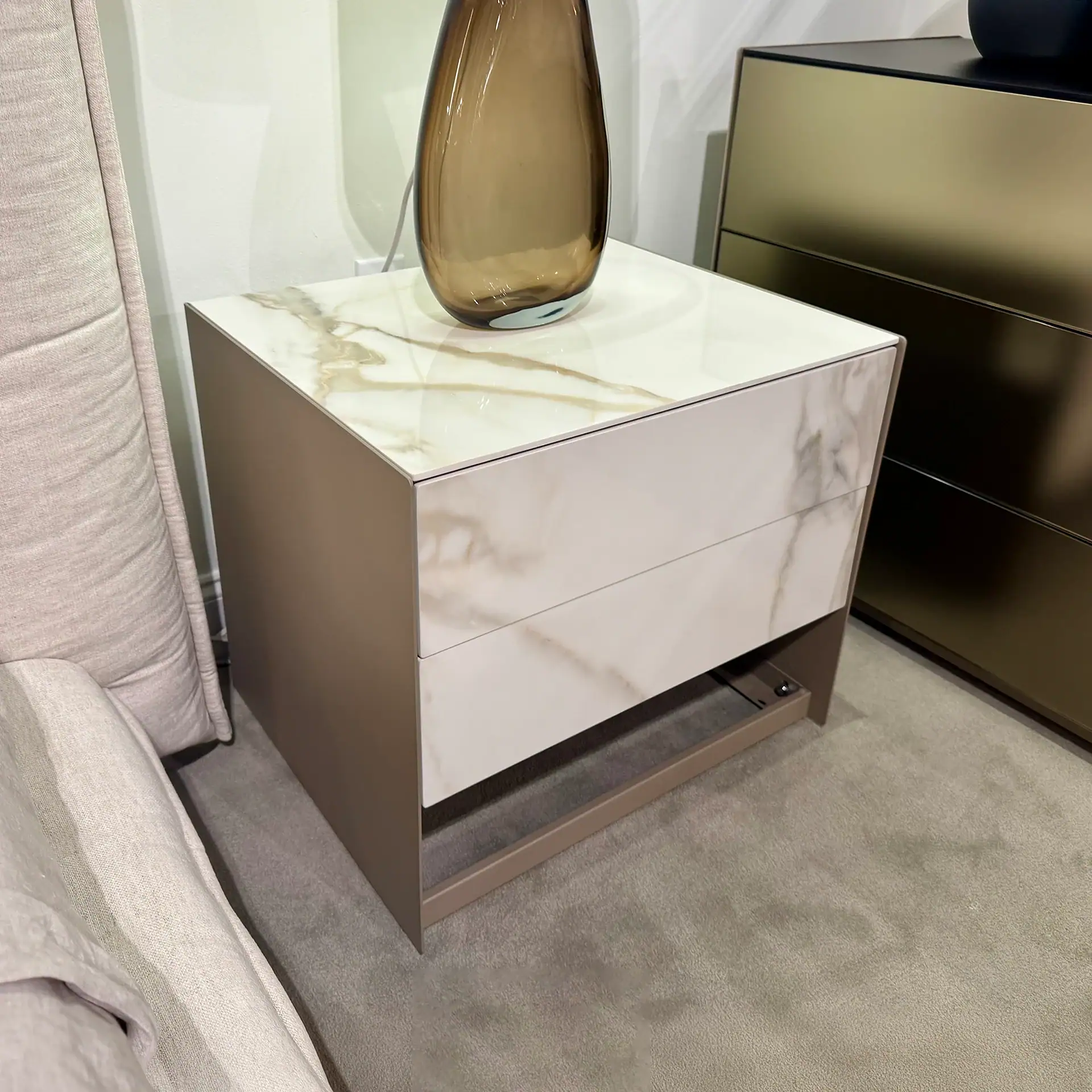 Modern nightstand with marble top and dark base in bedroom setting.