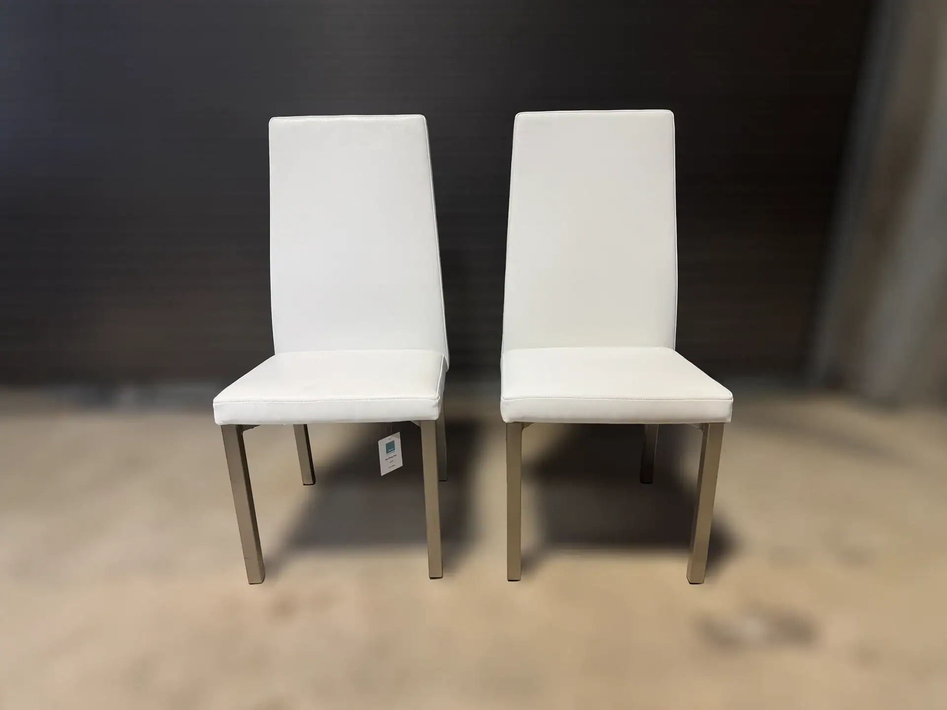 Pair of modern white dining chairs with wooden legs on showroom floor.