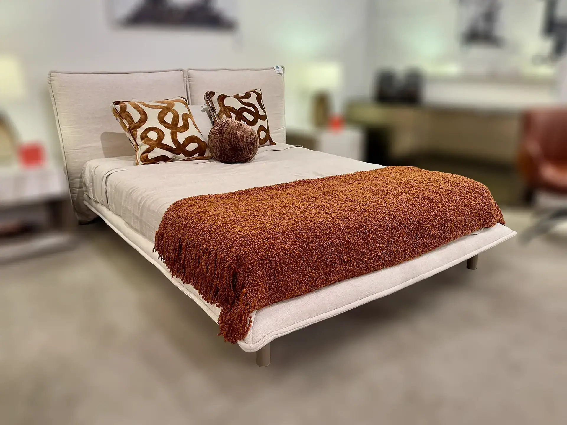 Trica Haven queen bed with beige upholstery and decorative pillows in a furniture store.