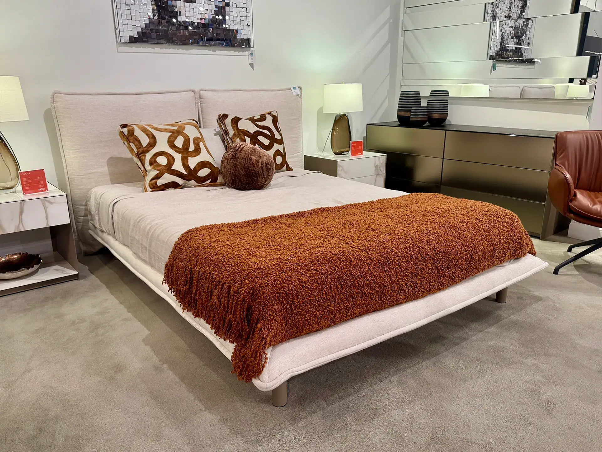 Modern queen bed with beige upholstery and decorative pillows in showroom.