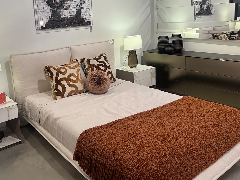 Modern queen bed with beige headboard and decorative pillows in bedroom setting.