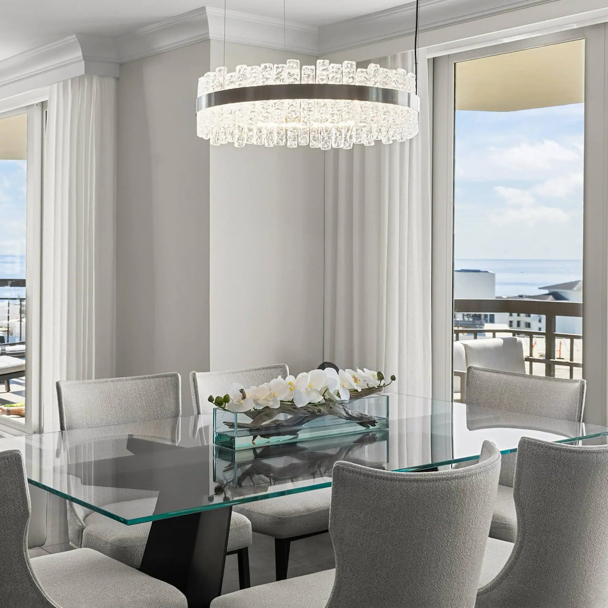 Luxurious dining room featuring a sleek glass table and comfortable chairs, with a stunning ocean vi.