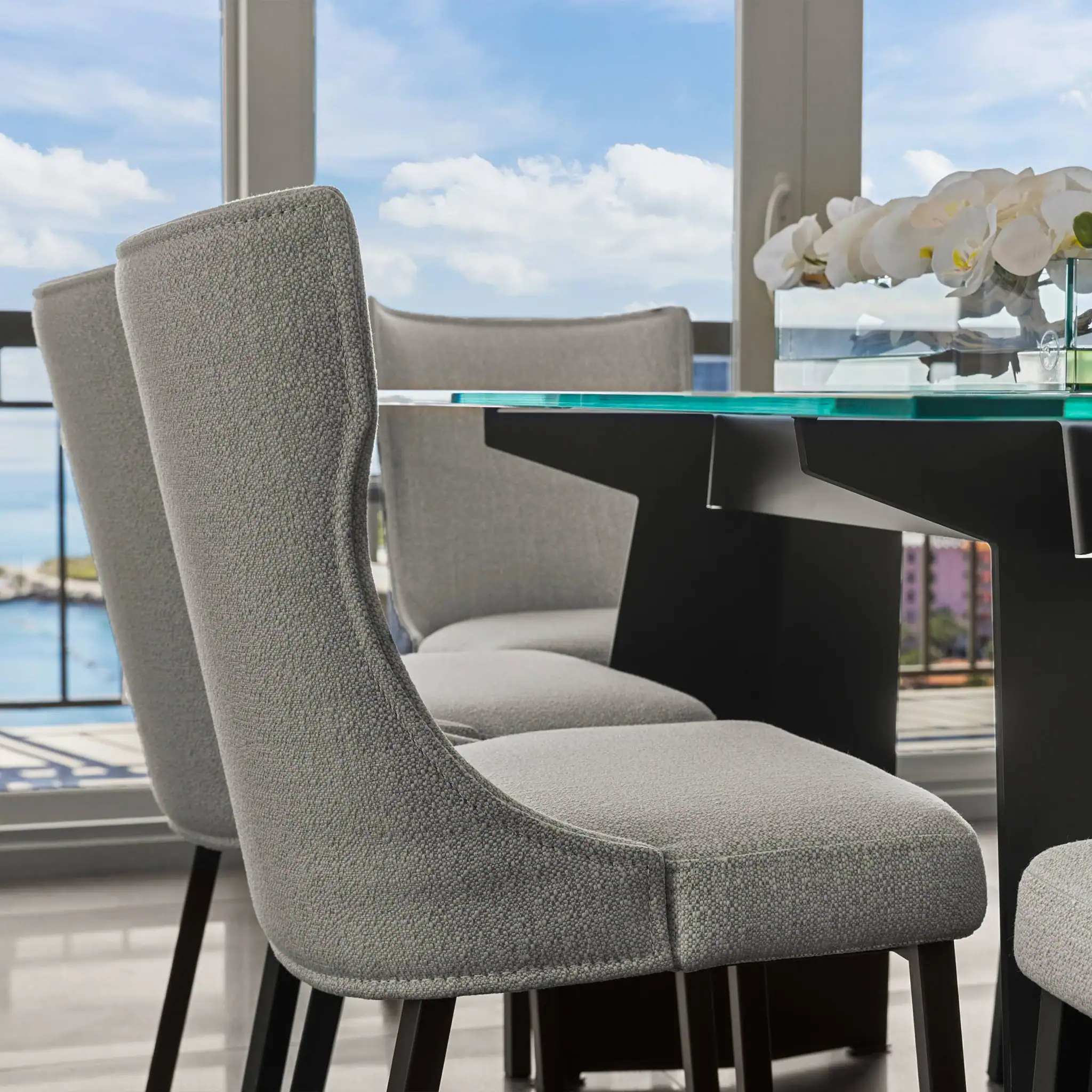 Elegant gray upholstered dining chairs around a glass table in a bright, modern dining room.