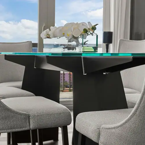 Contemporary glass dining table with floral centerpiece, surrounded by elegant chairs in a well-lit.