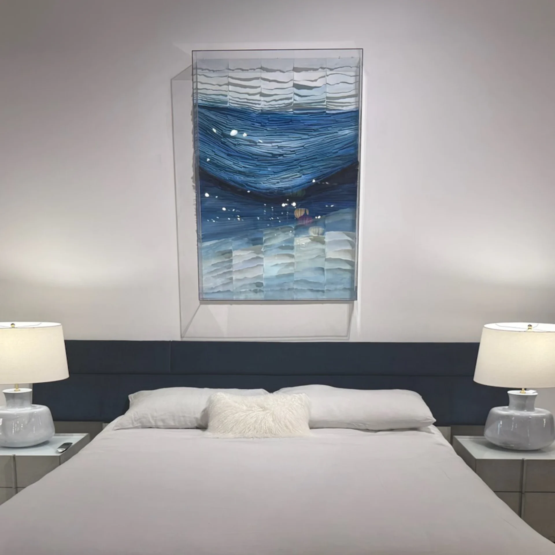 A modern bedroom with a bed, two nightstands, two lamps, and a large blue and white abstract artwork above the bed.