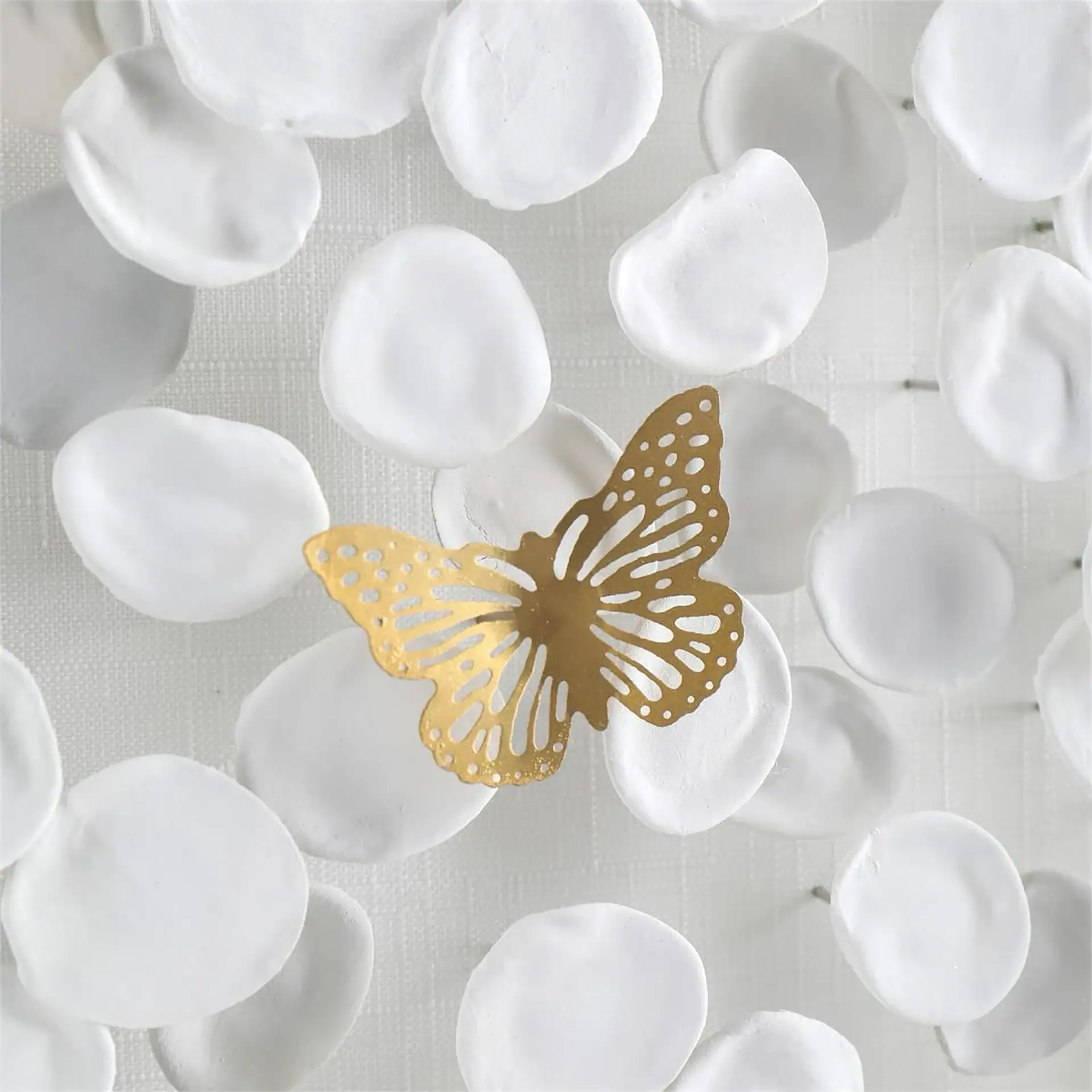 Gold butterfly ornament among white flower petals for home decor.