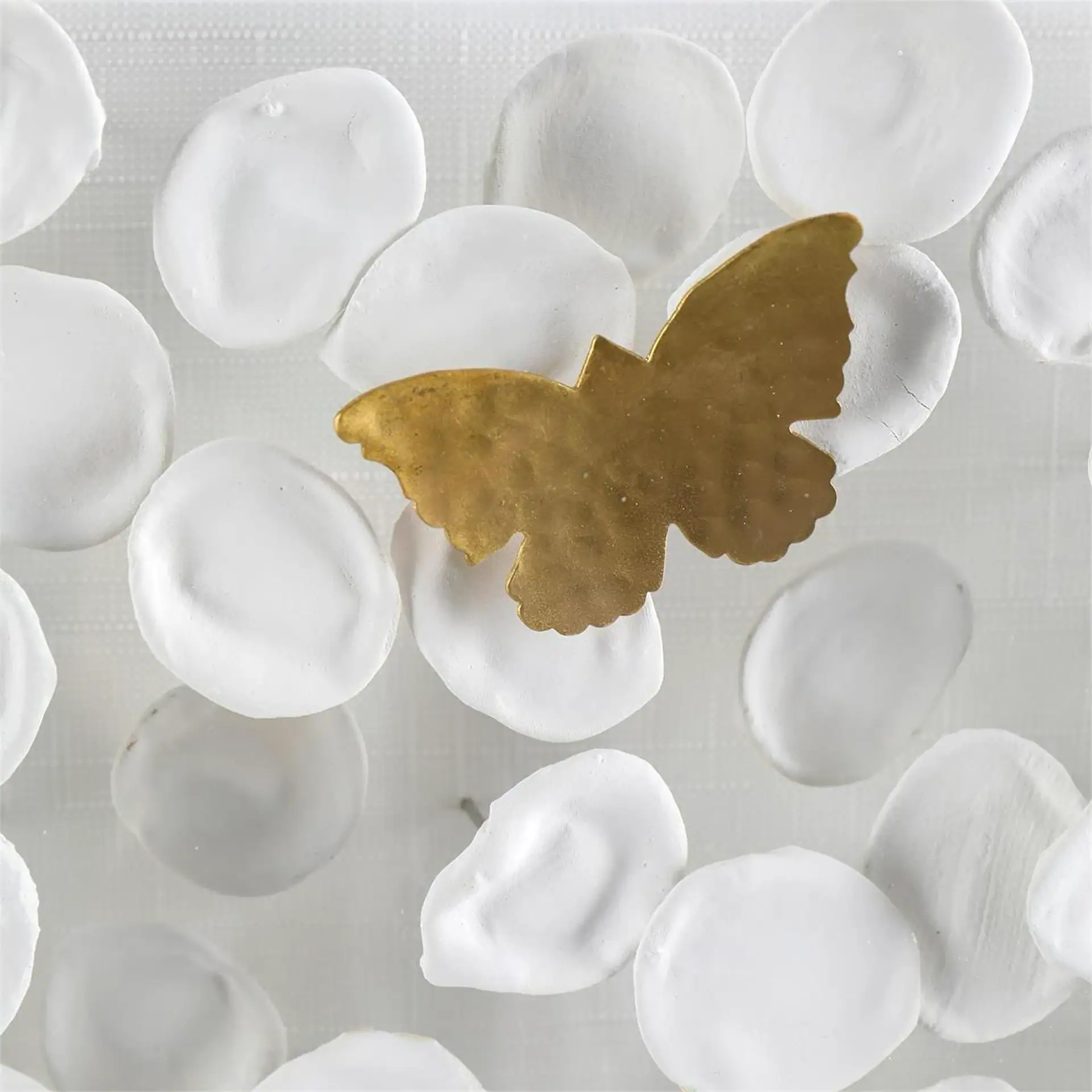 Gold butterfly ornament on white flower petals for home decor.