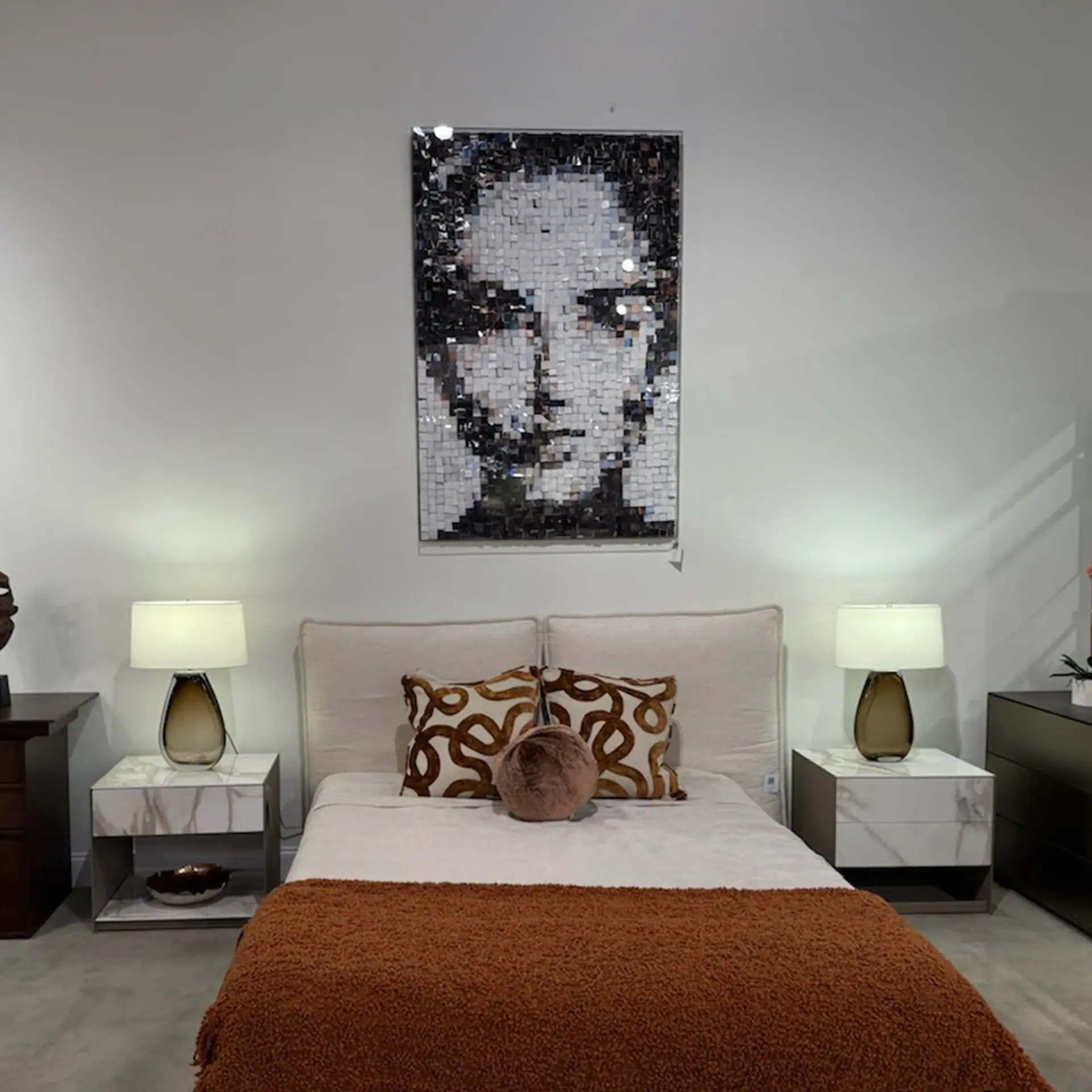 Contemporary bedroom featuring mosaic portrait art, white bedding, and elegant nightstands.